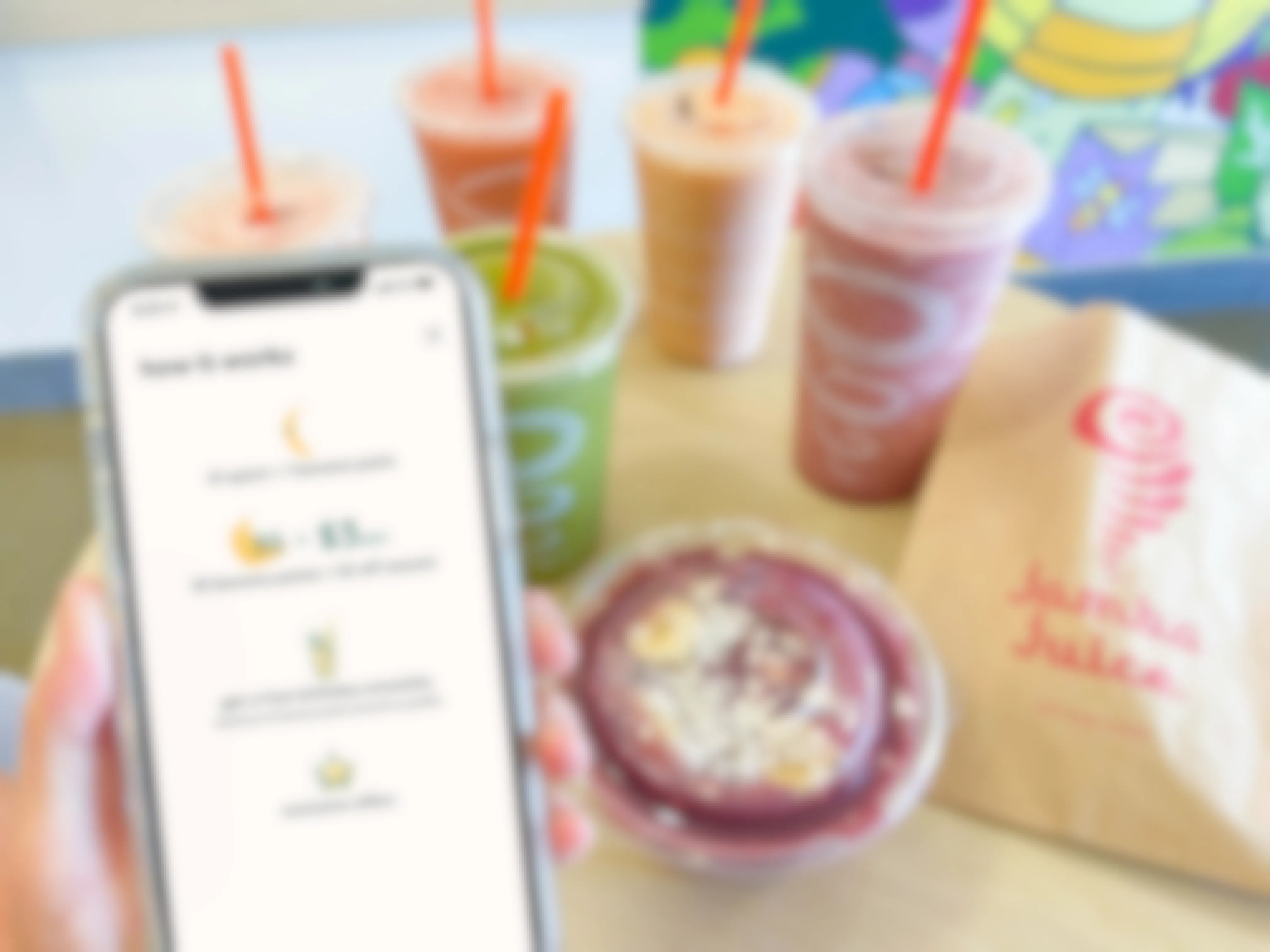 woman holding cellphone with rewards info near table full of jamba juice 