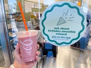 holding a smoothie on one hand and birthday smoothie reward sign