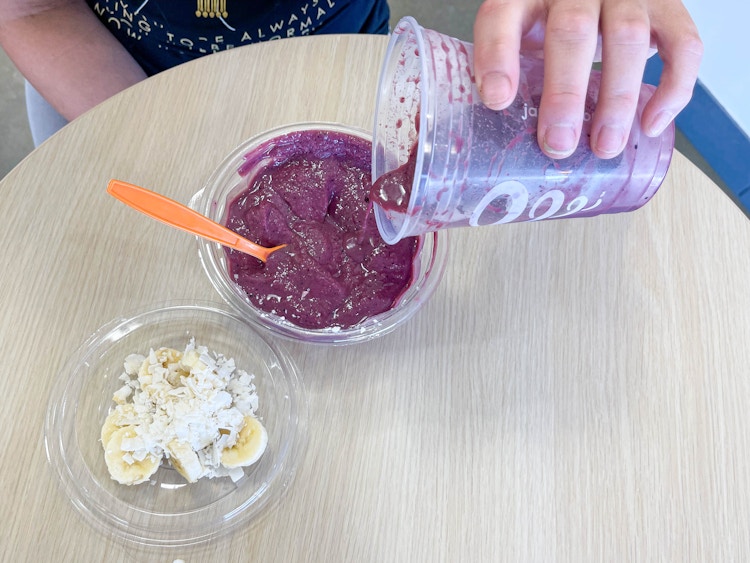 pouring an acai smoothie into a bowl with toppings 
