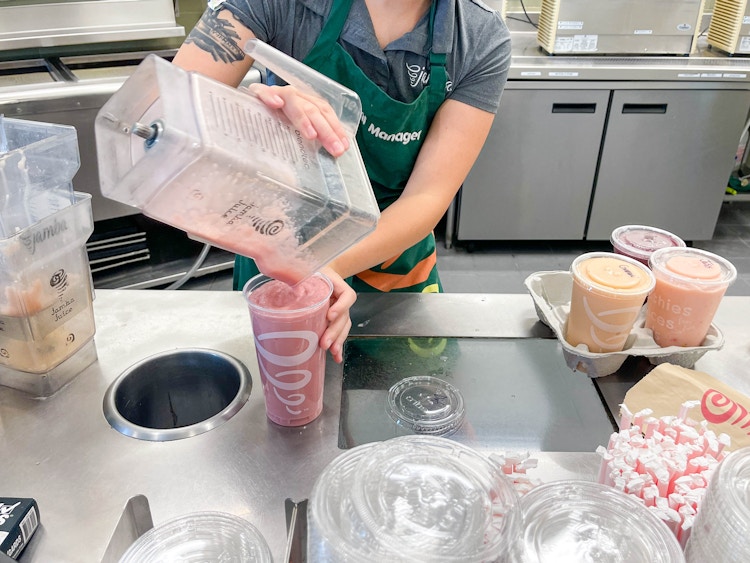 employee pouring jamba juice smoothie into large cup 
