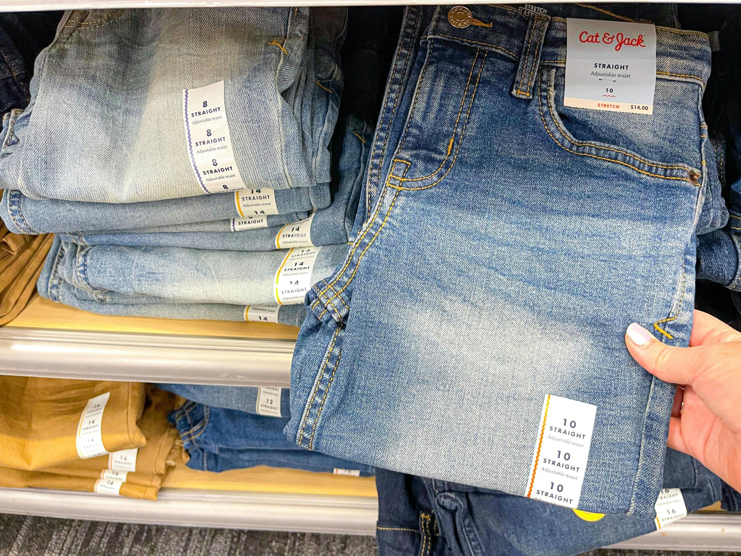 A person taking a pair of Cat and Jack straight fit jeans from a shelf at Target.