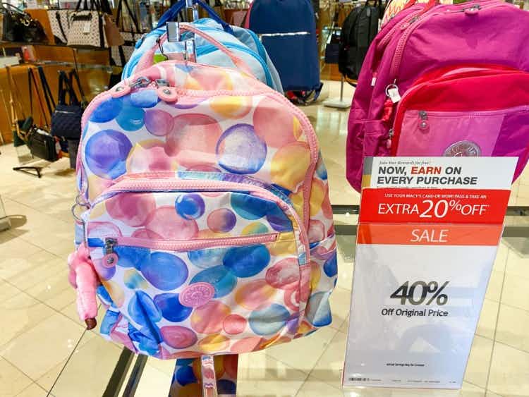 a multi-colored kipling backpack next to a sale sign