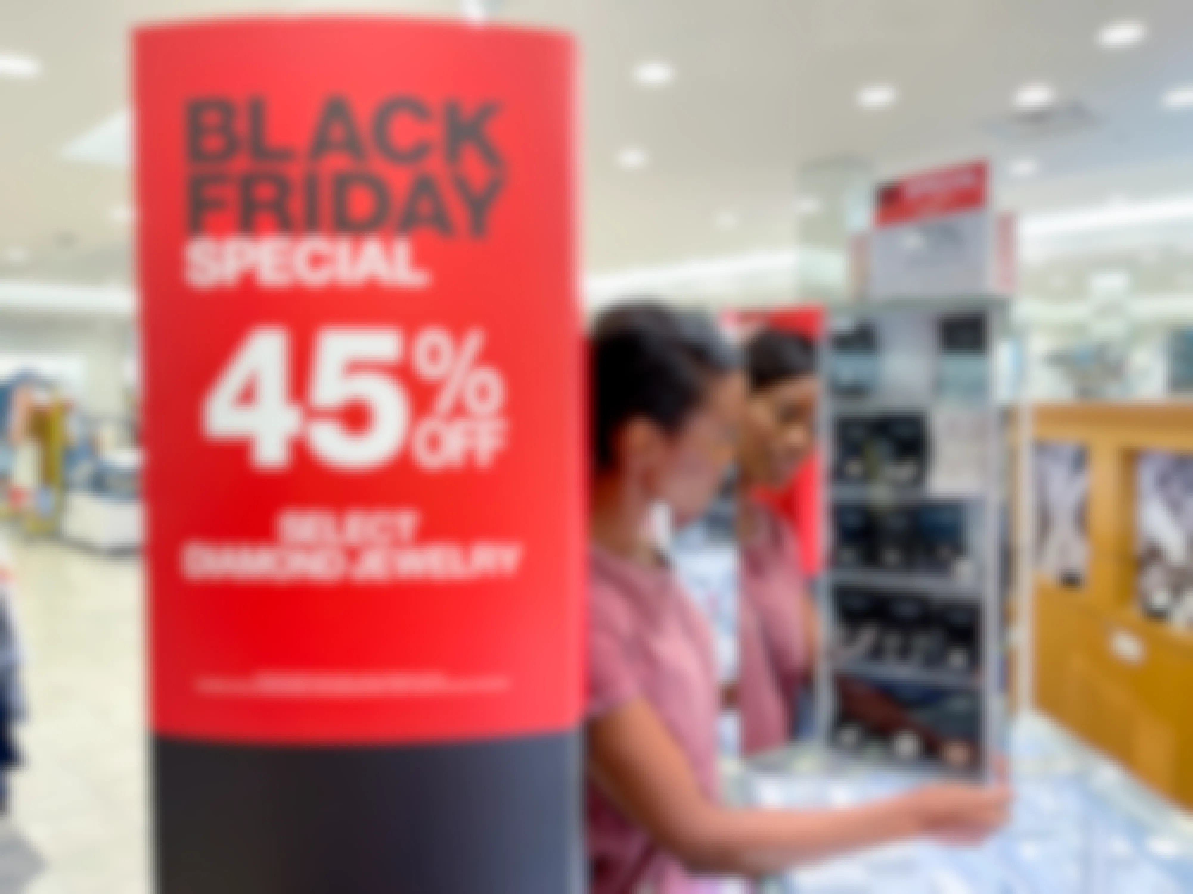 A 45% off Black Friday sign in a Macy's store next to a person looking at a display on the jewelry counter.