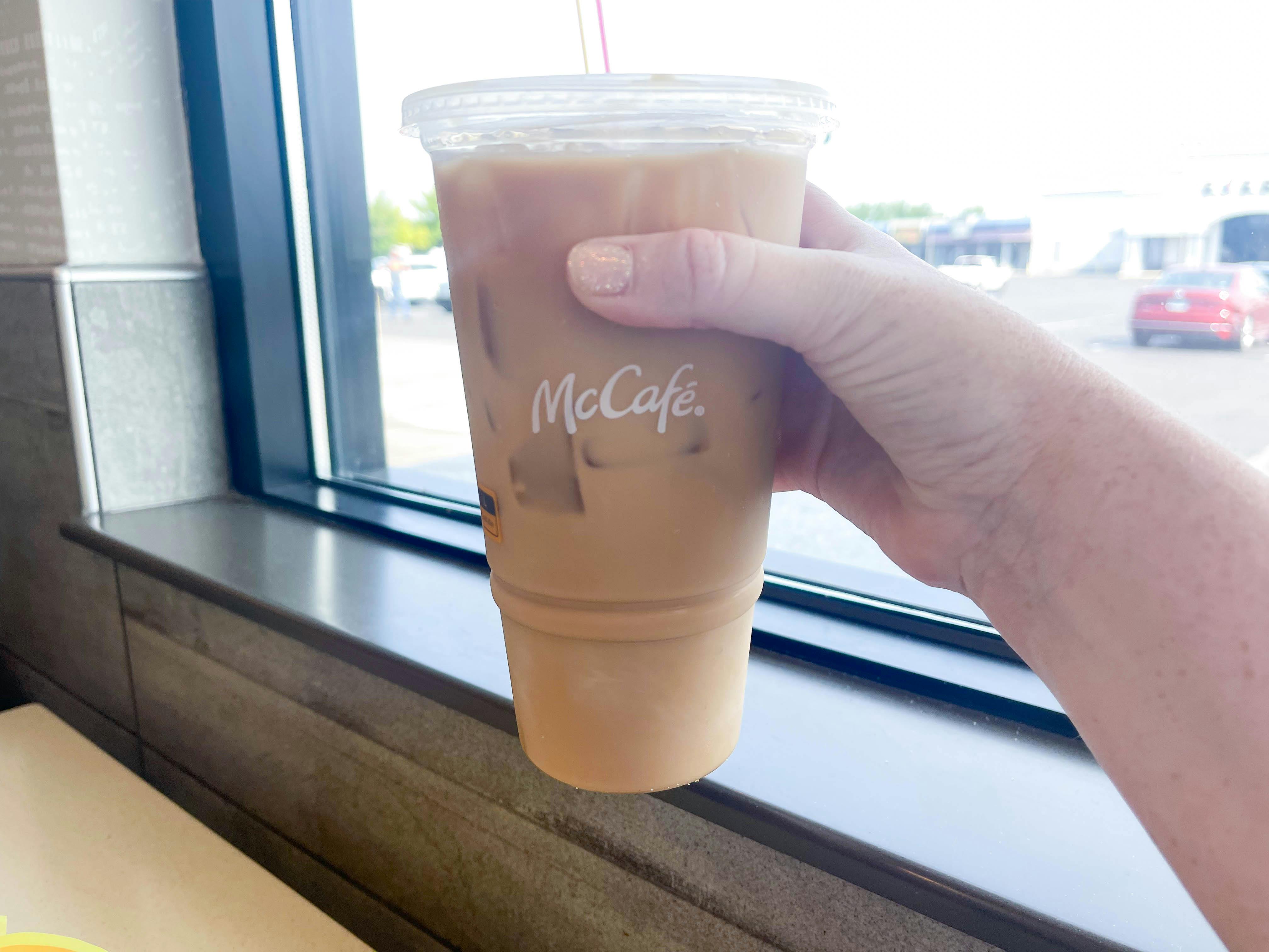 a large iced coffee from mccafe being held in front of window