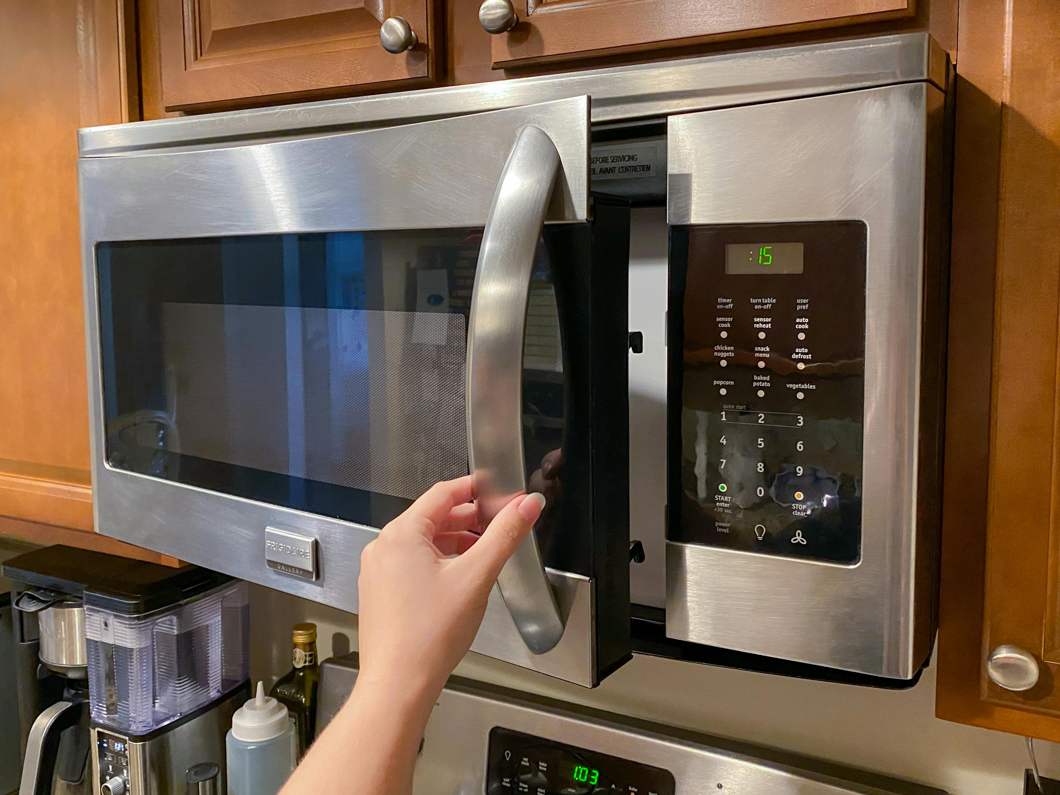 A person's hand opening the door of a mounted microwave.