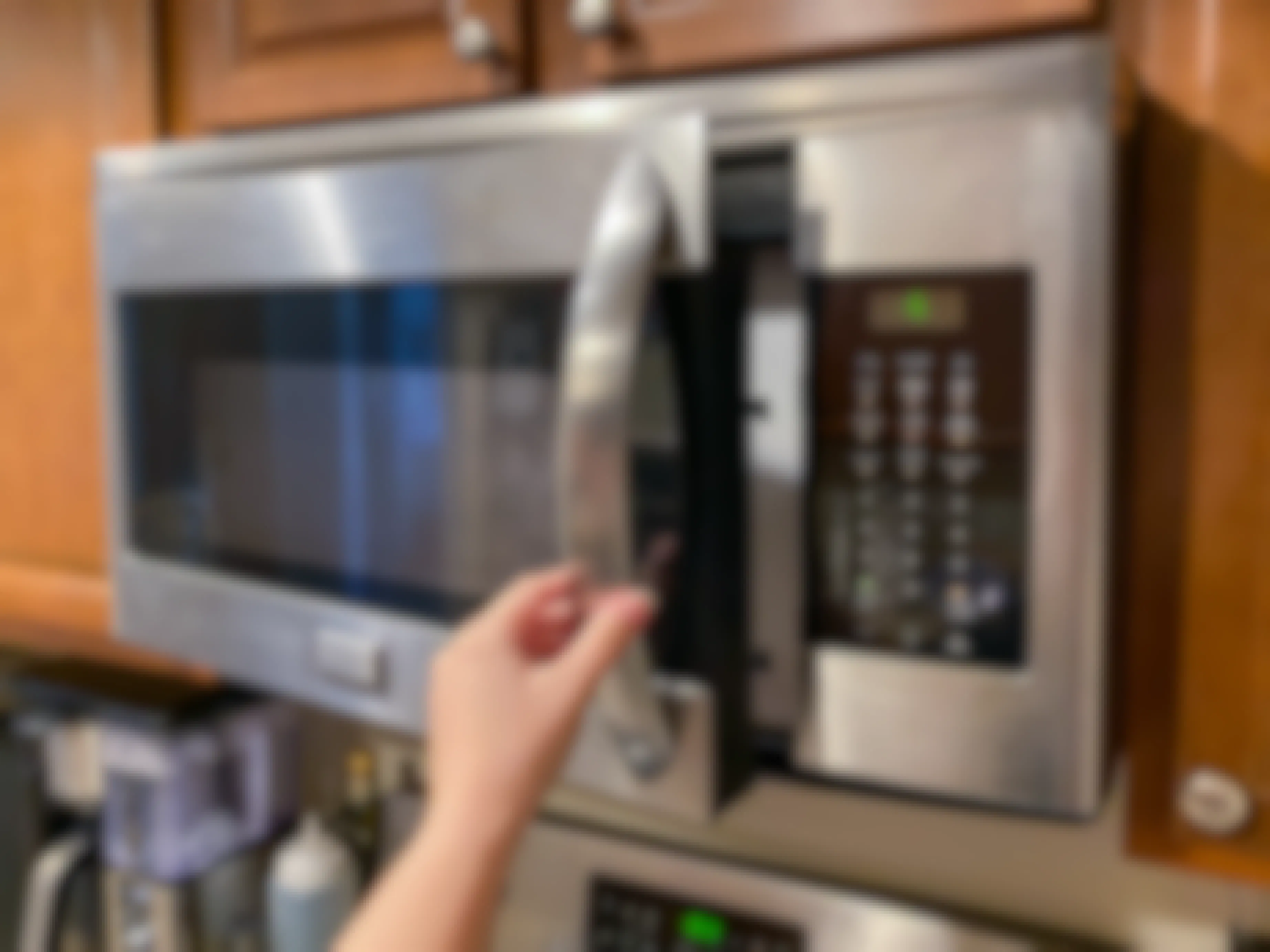 A person's hand opening the door of a mounted microwave.