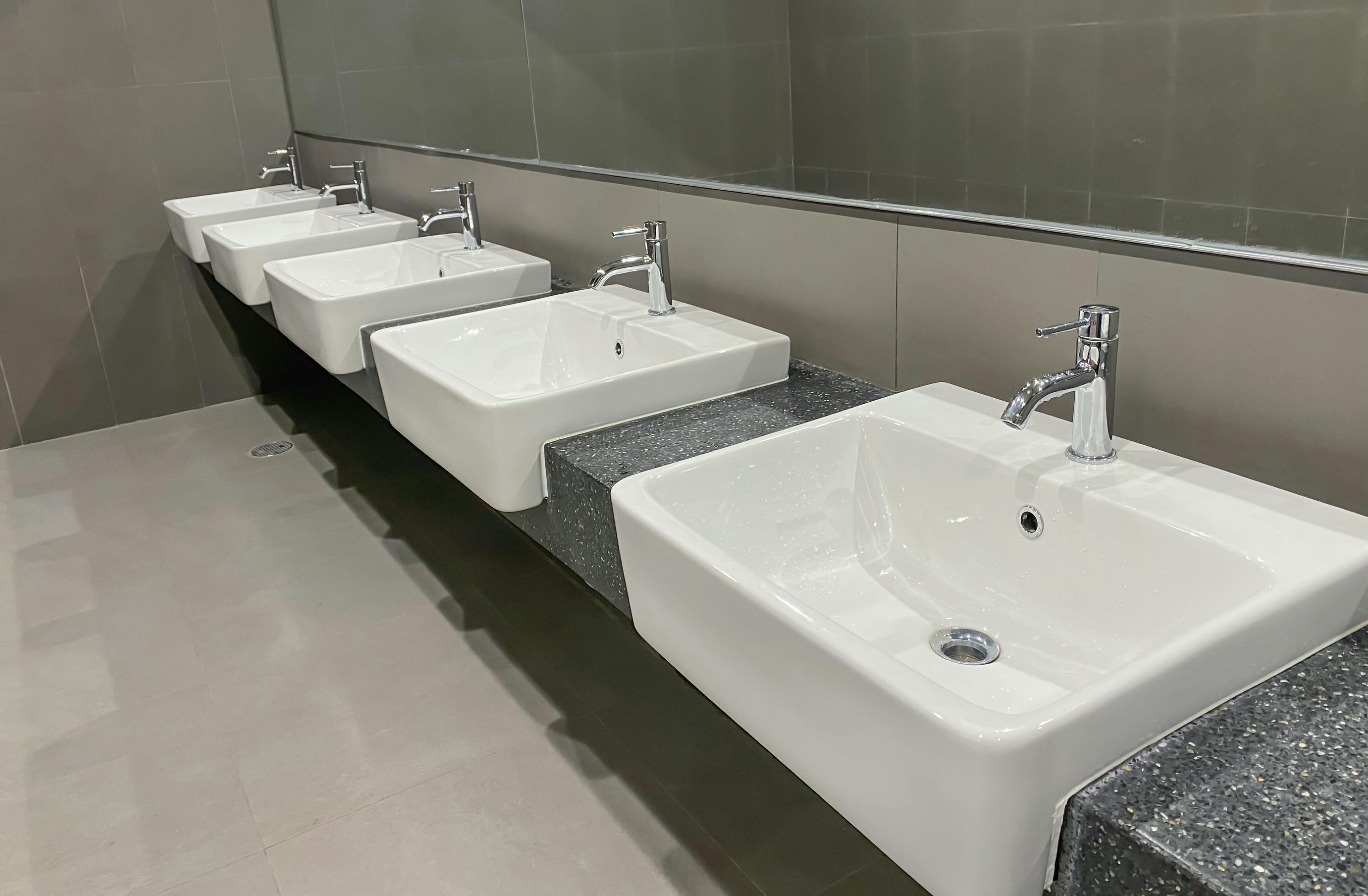 A line of white counter sinks in a public restroom