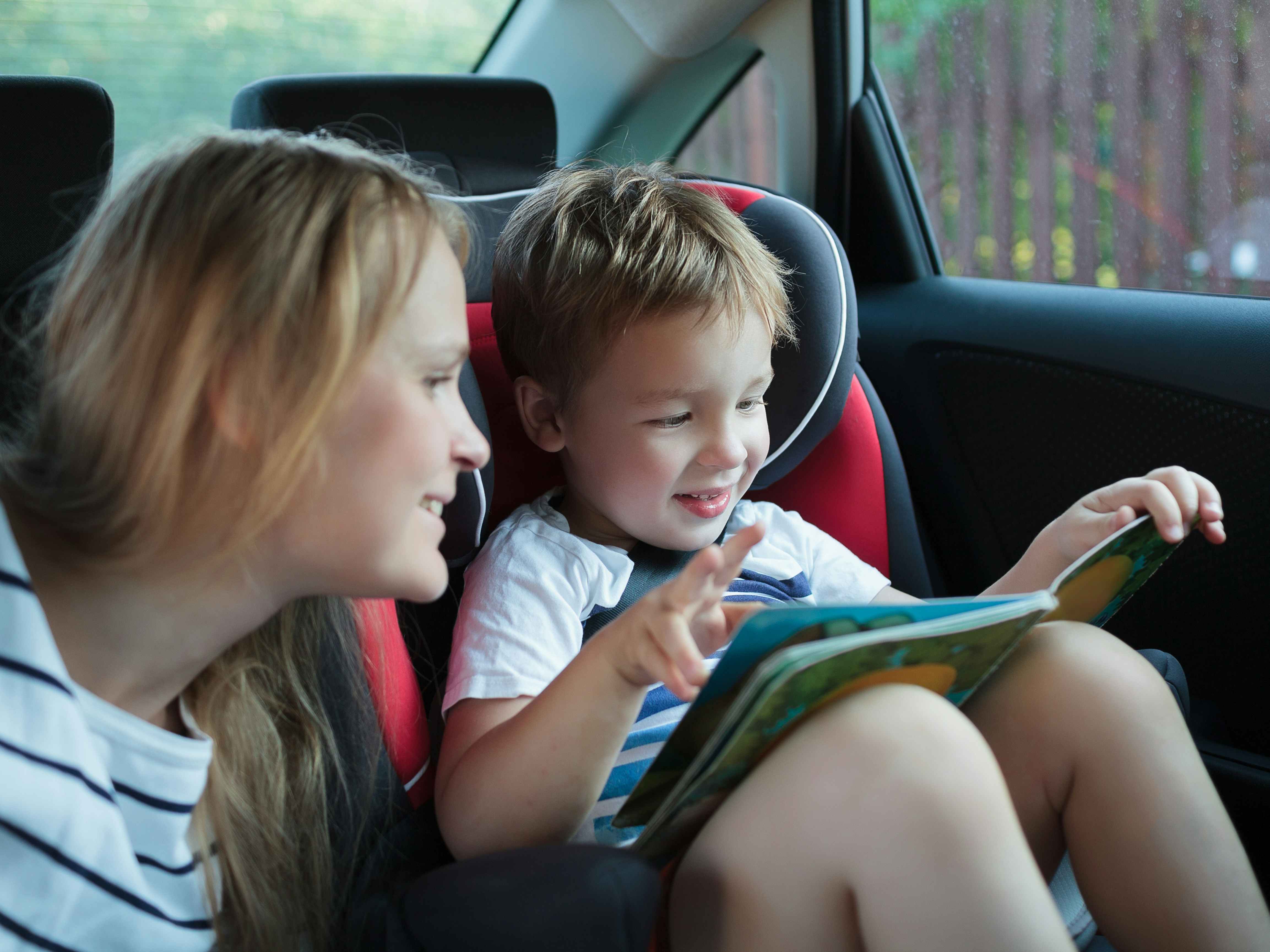 A mother and her child in the back seat of a vehicle, looking at a children's book