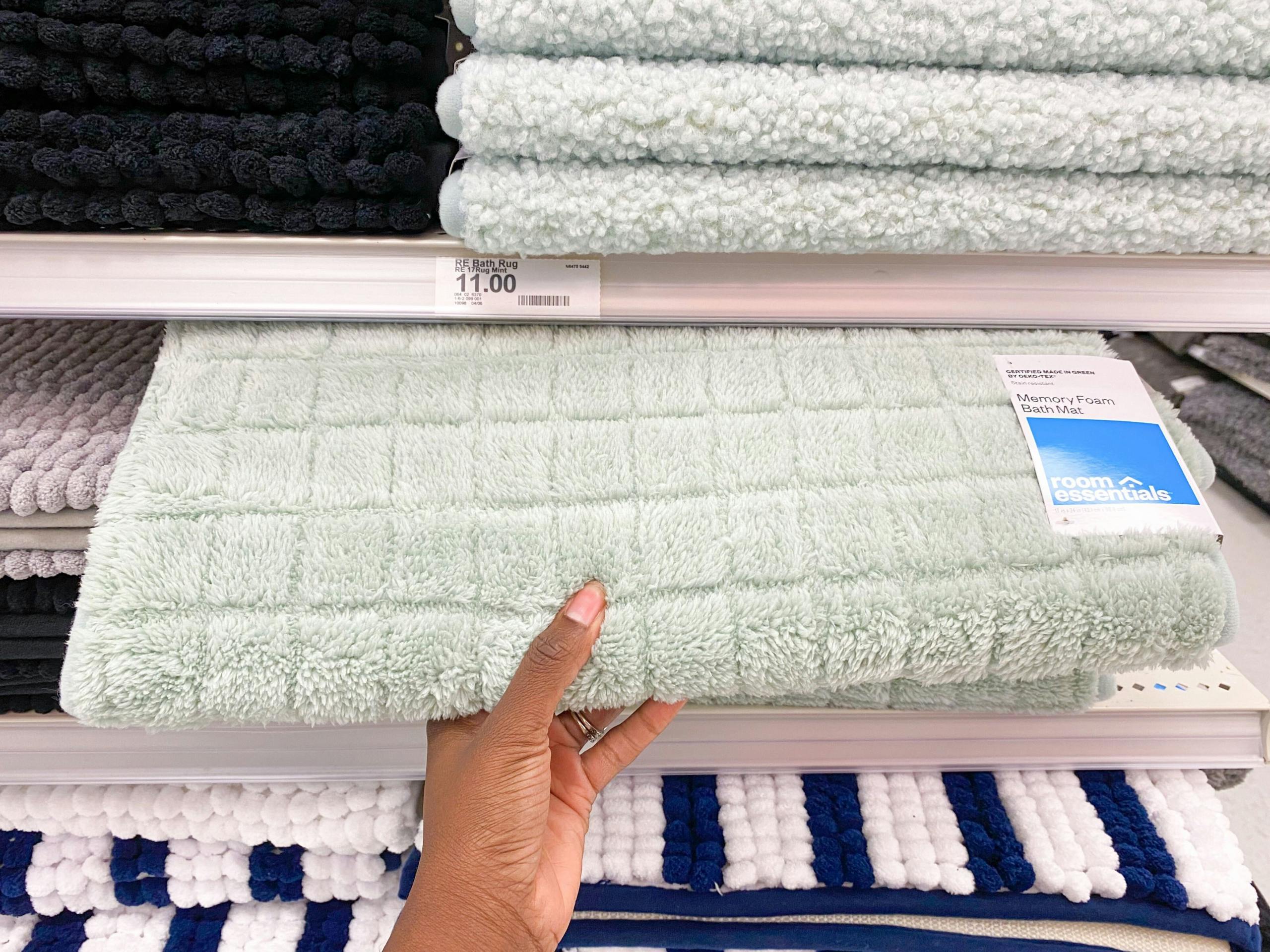 A person's hand taking a memory foam bath rug from a Target shelf.