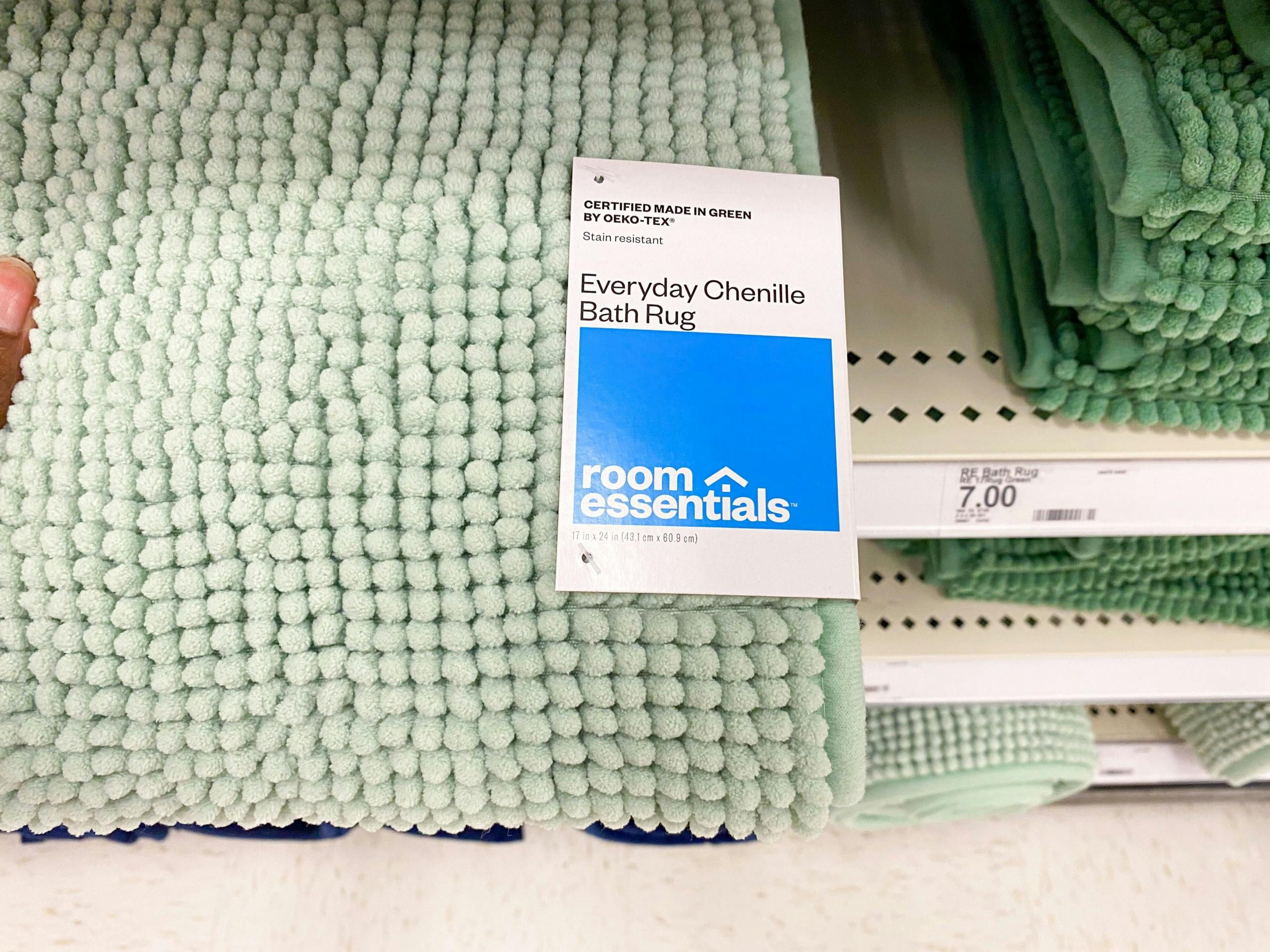 A person's hand taking a Room Essentials everyday chenille bath rug from a shelf at Target.