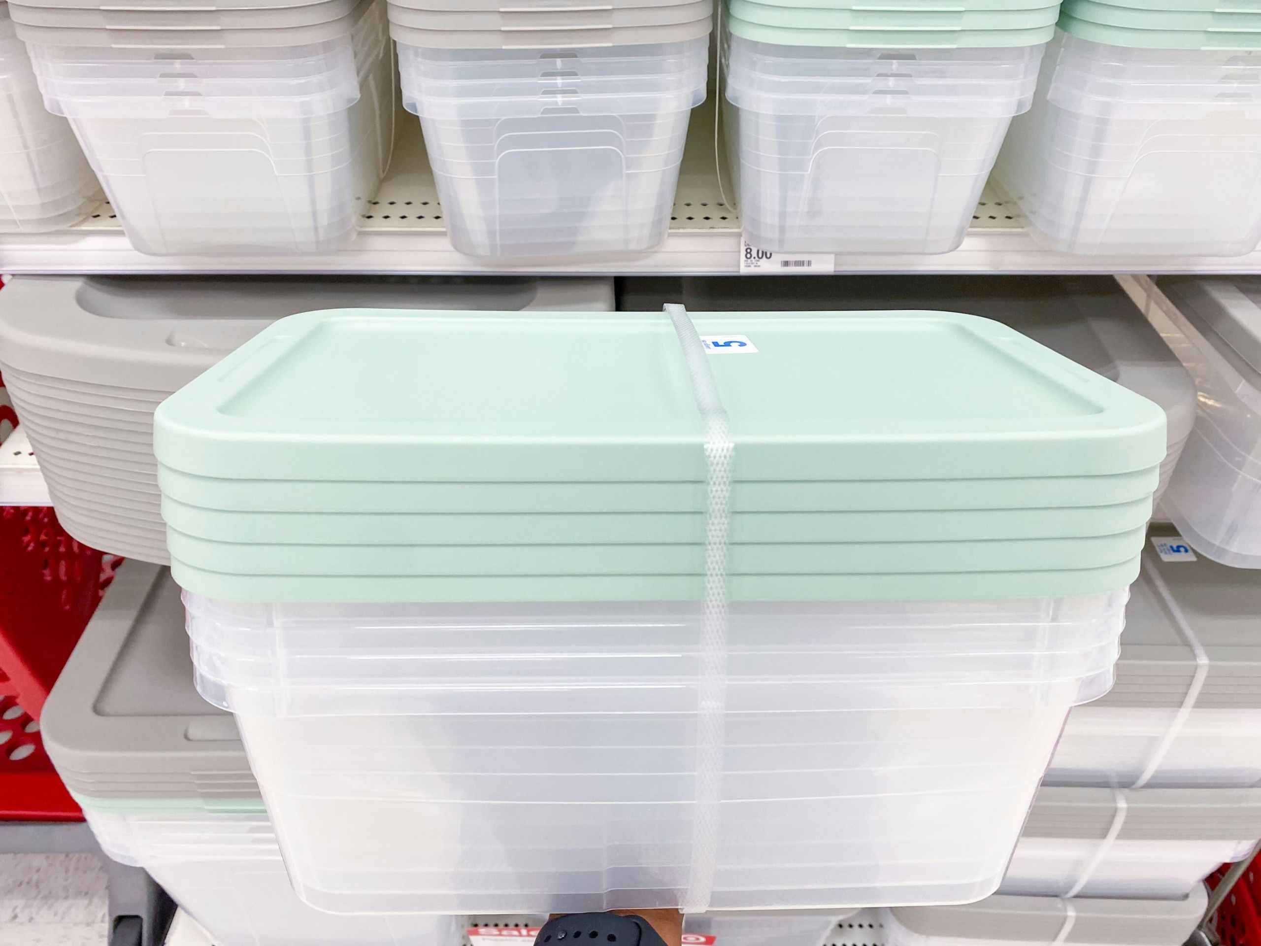 hand holding a 5-pack of 6-quart storage boxes in front of a target shelf