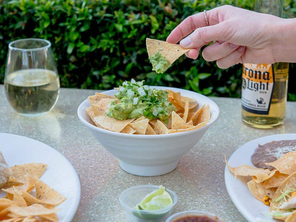 A person's hand dipping a chip into a bowl of guacamole on a table at Rubio's.