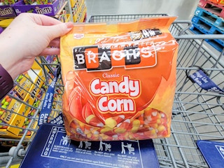 hand holding a large bag of candy corn in a cart