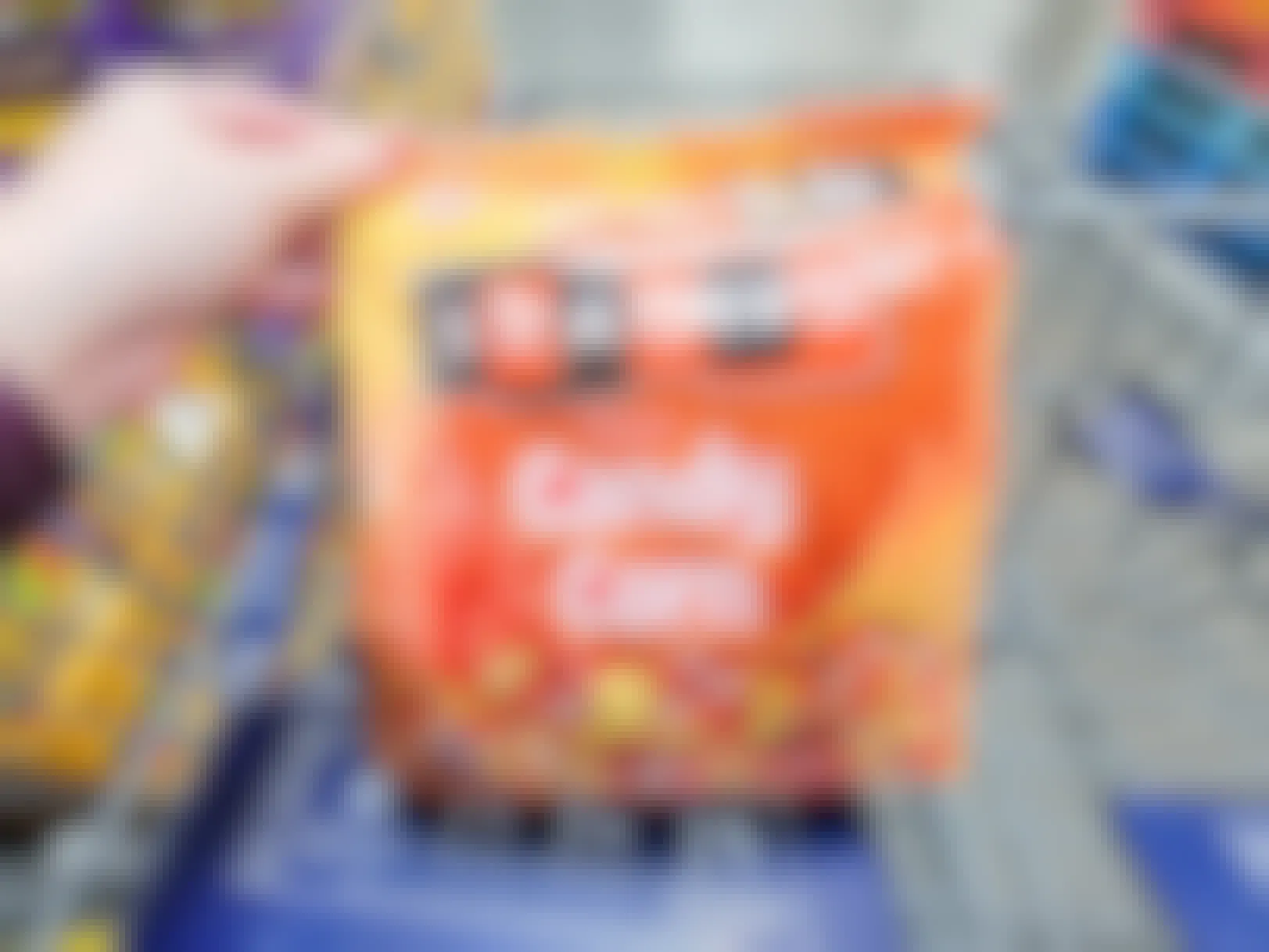 A person's hand putting a large bag of candy corn in a cart at Sam's Club.