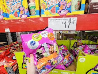 hand holding a large bag of assorted hersheys halloween candy icnlduing york peppermint patties, kit kat, reese's etc