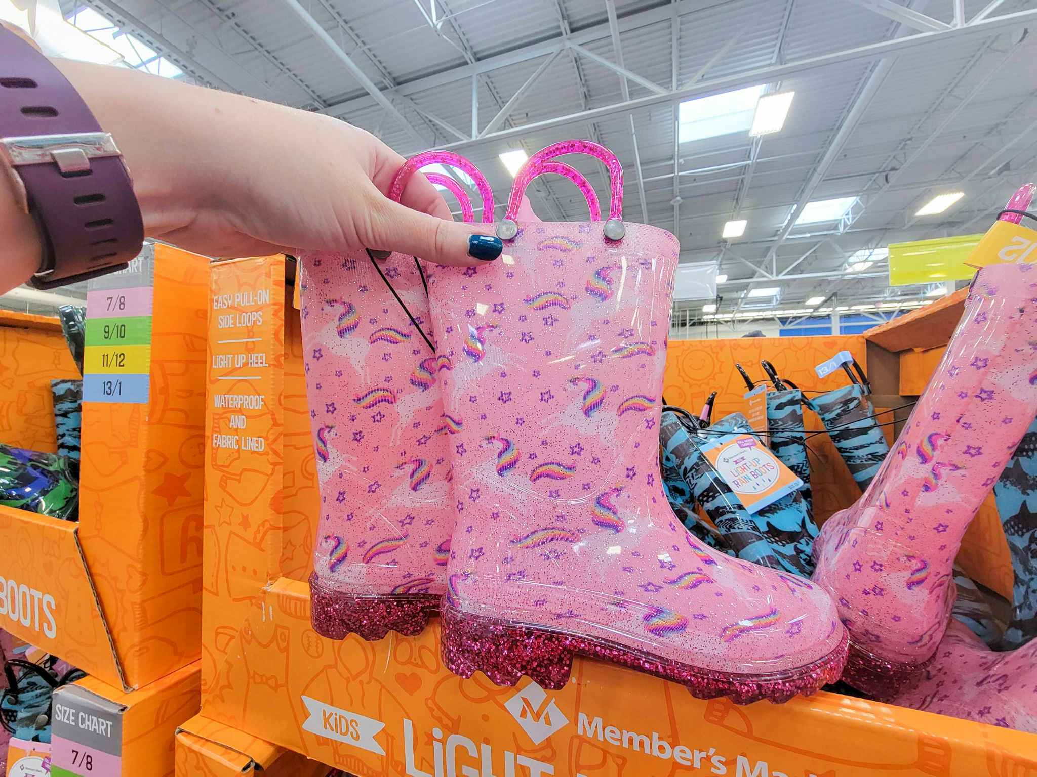 hand holding pink light up rain boots with unicorns and rainbows