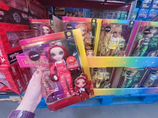 hand holding a rainbow high doll with red hair in front of other rainbow high dolls