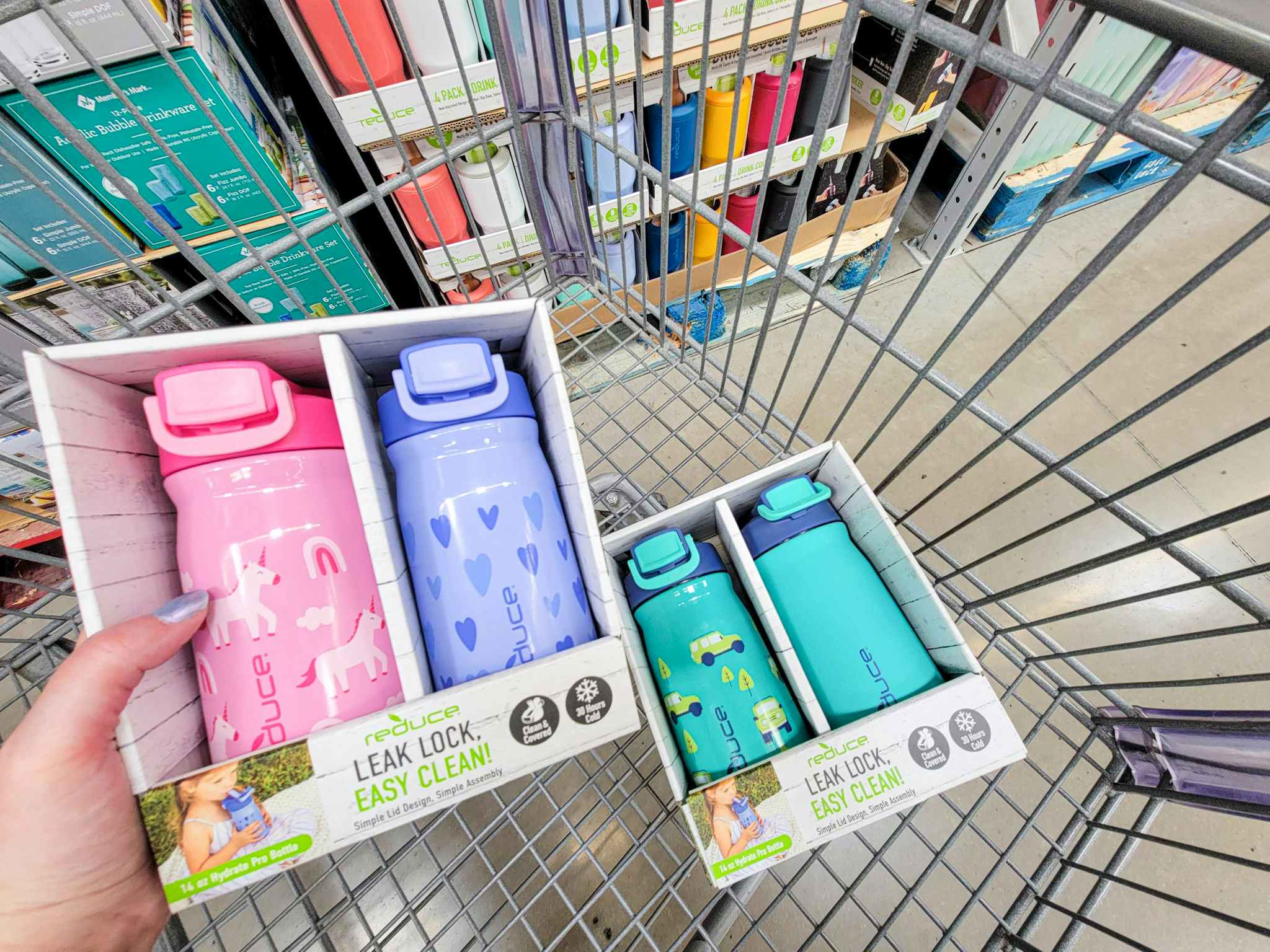 hand holding a 2 pack of kids water bottles, over a cart with another pack