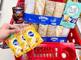 A target shopping cart containing kleenex 4 packs, a box of moonshot crackers, pedigree dog food packs, and blue diamond almond extremes