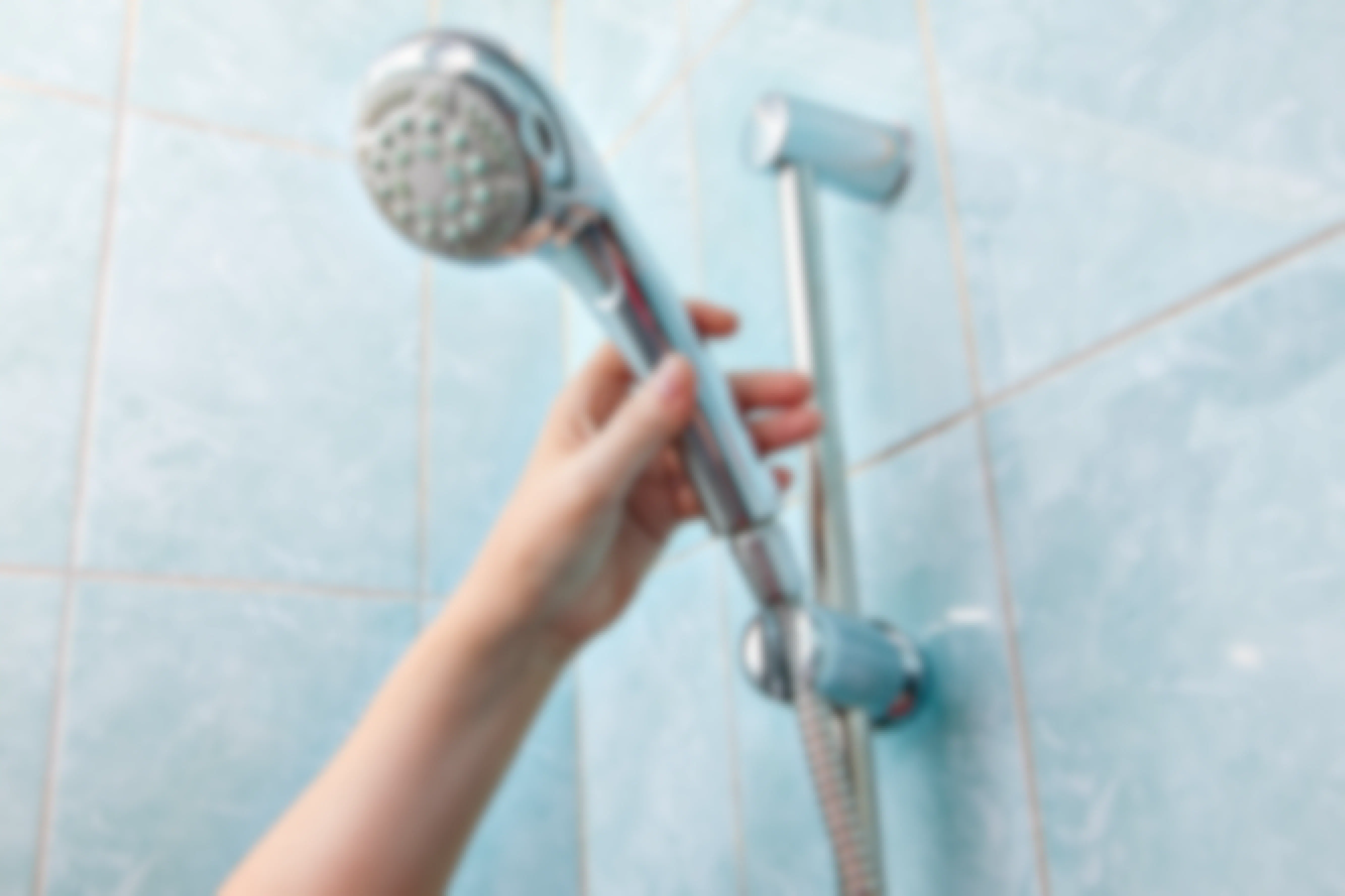 A person's hand reaching up to a shower head with a hose.