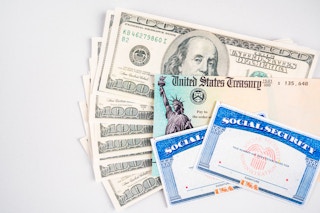 A stack of hundred dollar bills, a check from the US Treasury, and two blank Social Security cards.