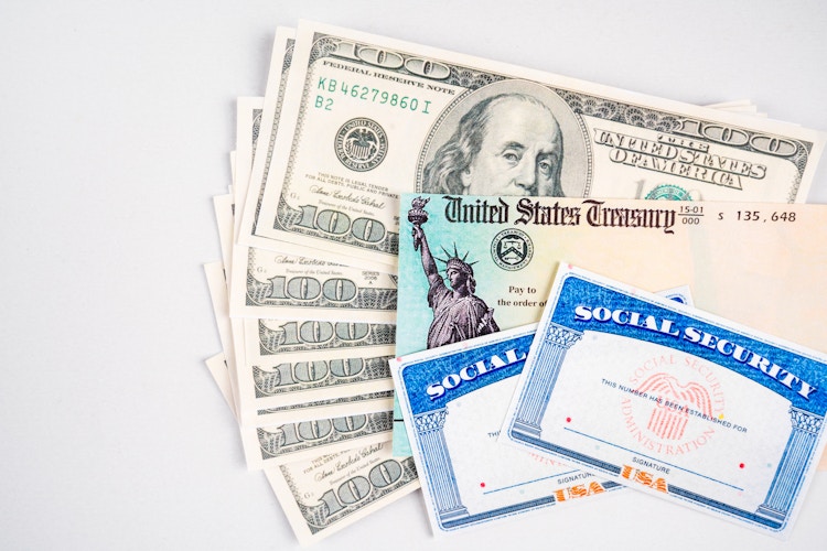 A stack of hundred dollar bills, a check from the US Treasury, and two blank Social Security cards.