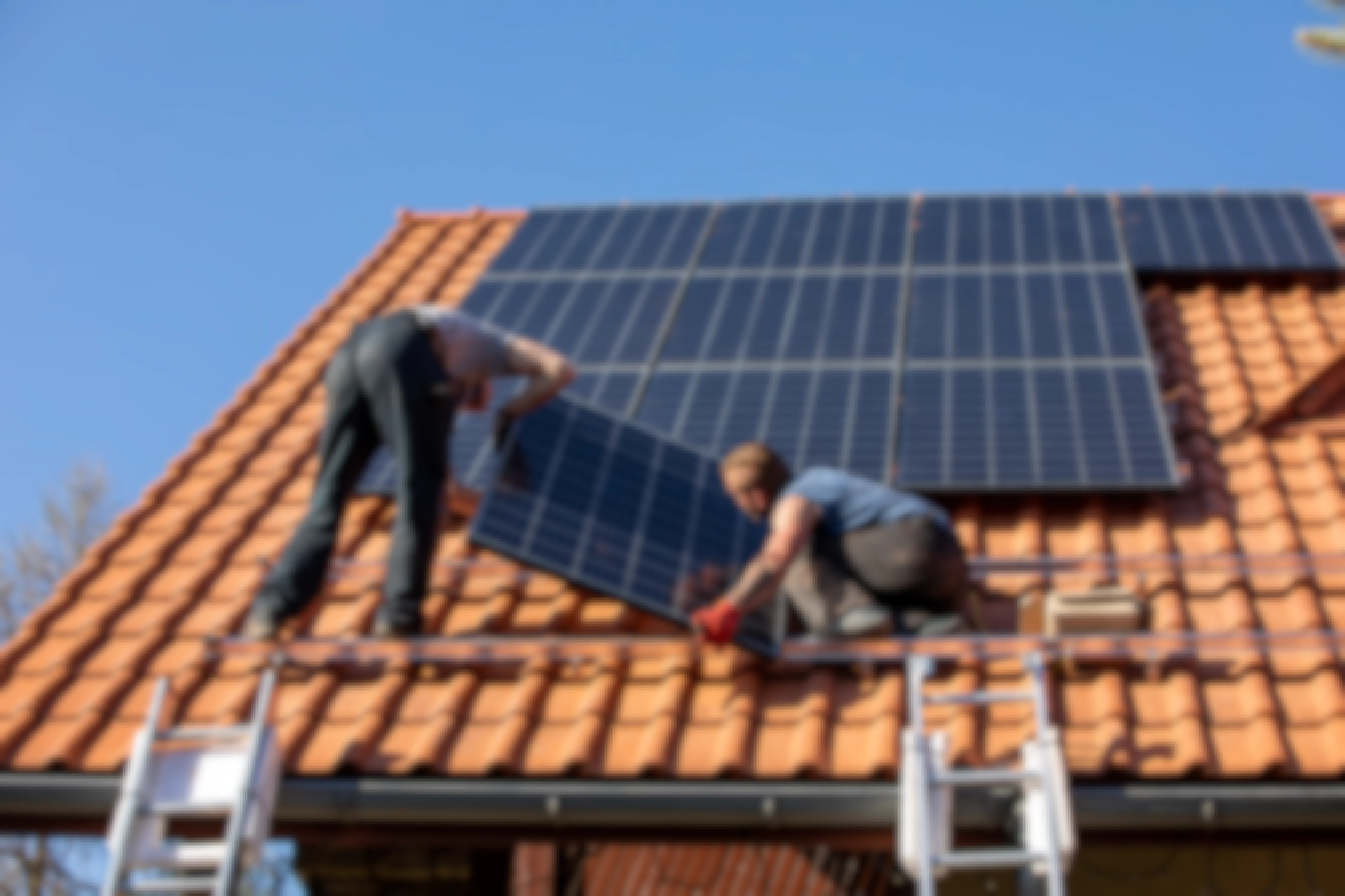 Two men installing solar panels onto the roof of a house.