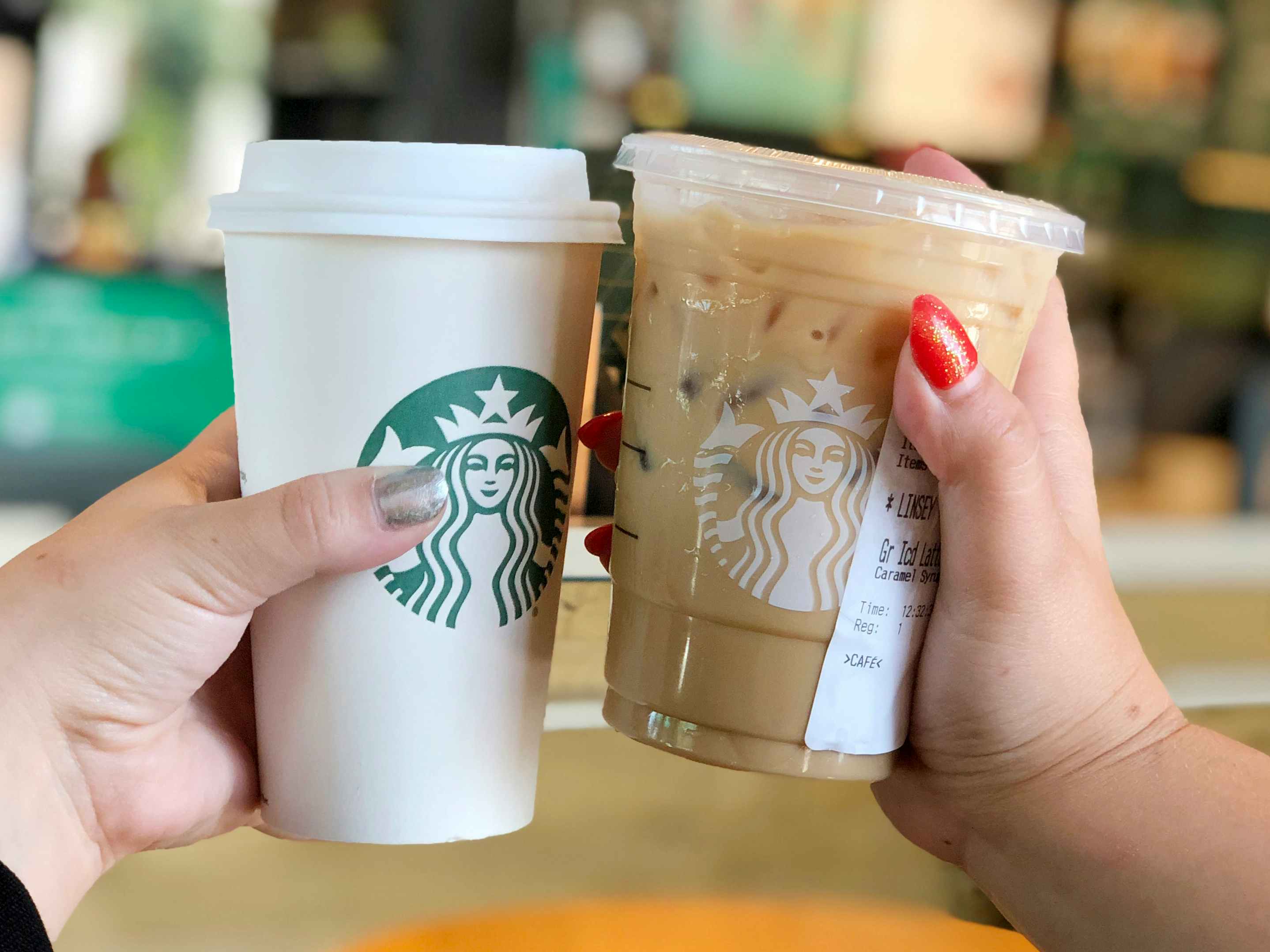 Two people's hands holding two Starbucks drinks up together.