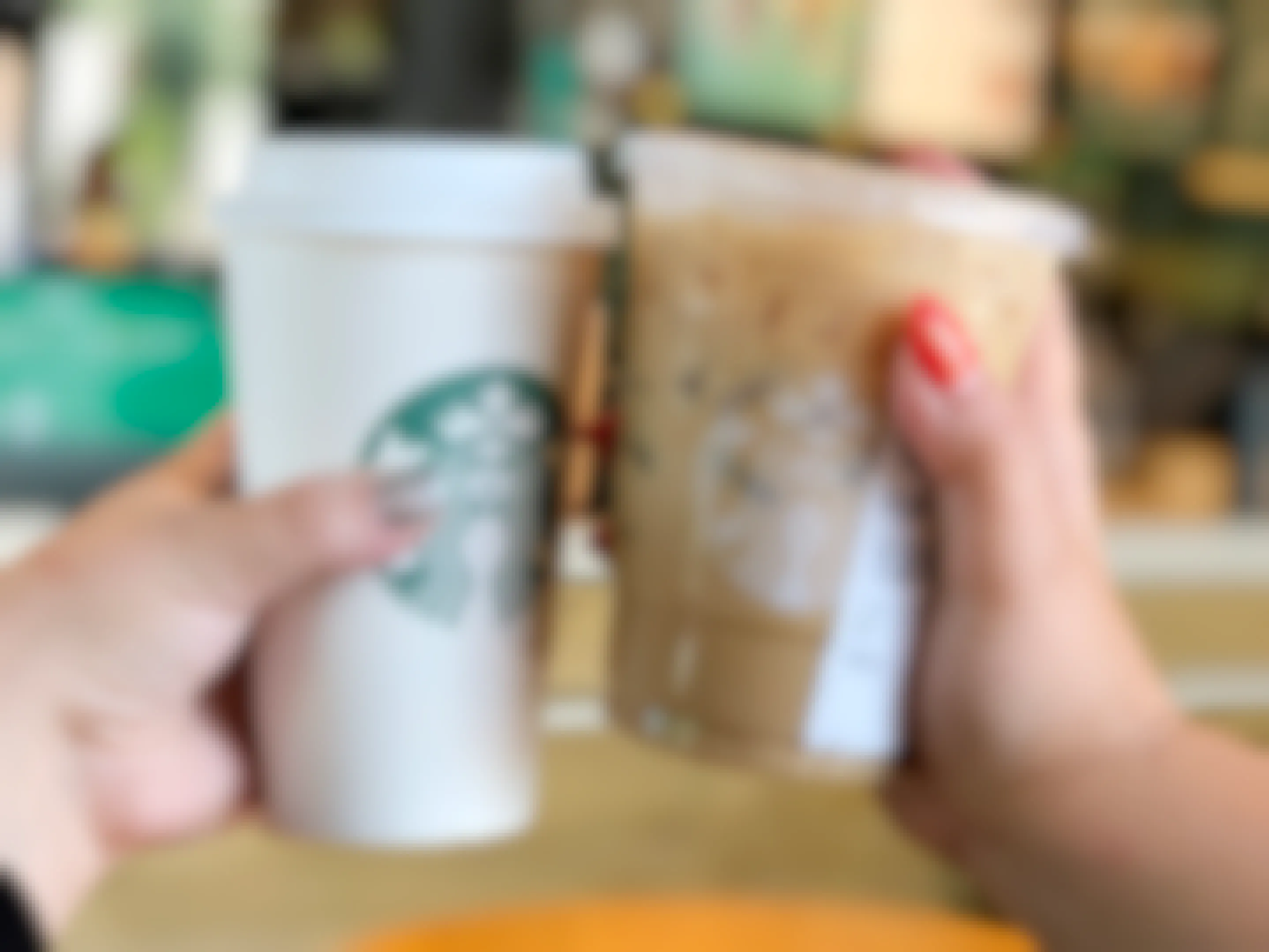 Two people's hands holding two Starbucks drinks up together.