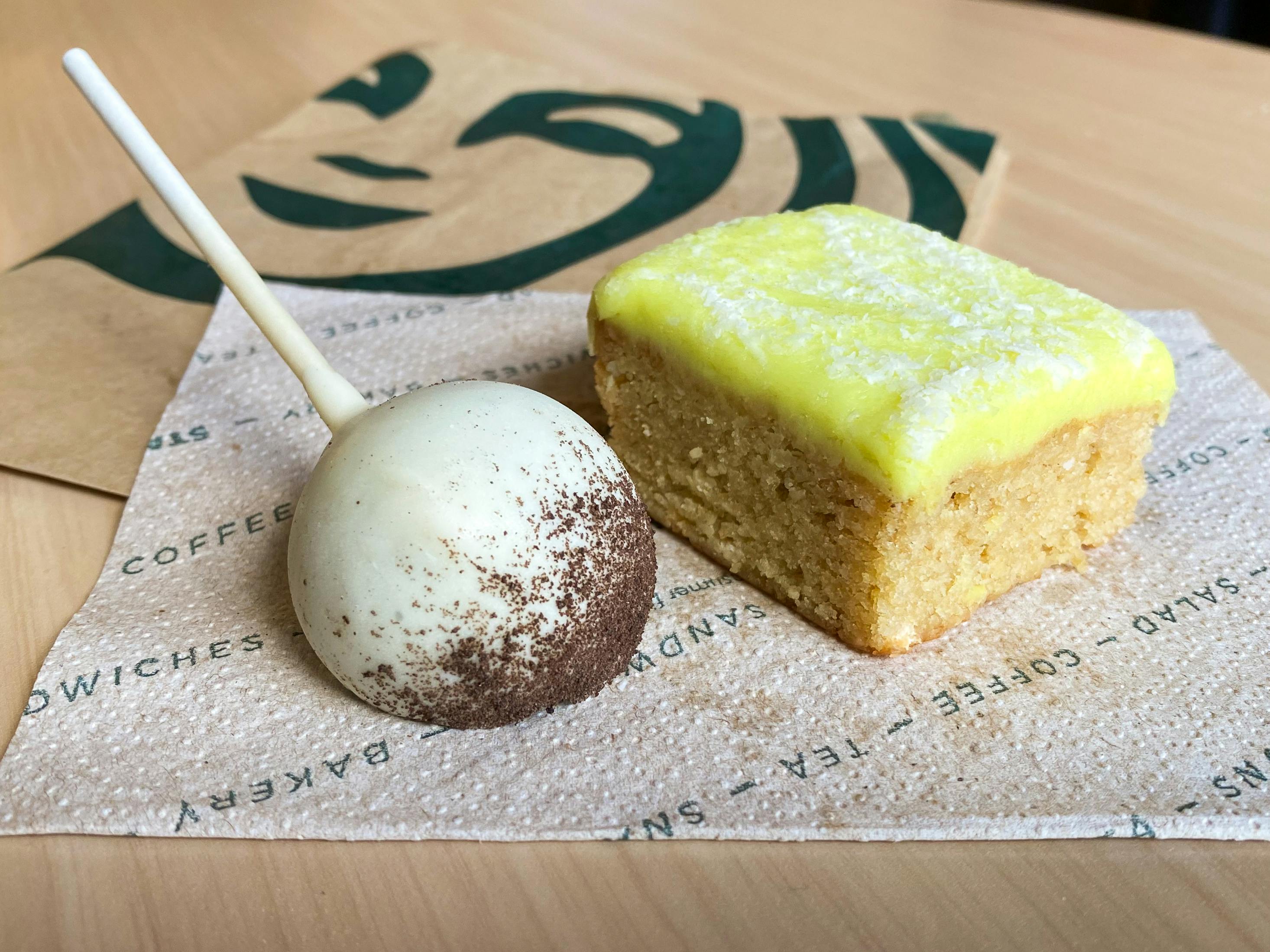 A cookies and cream cake pop and lime-frosted cake square sitting on a napkin on a table at Starbucks.