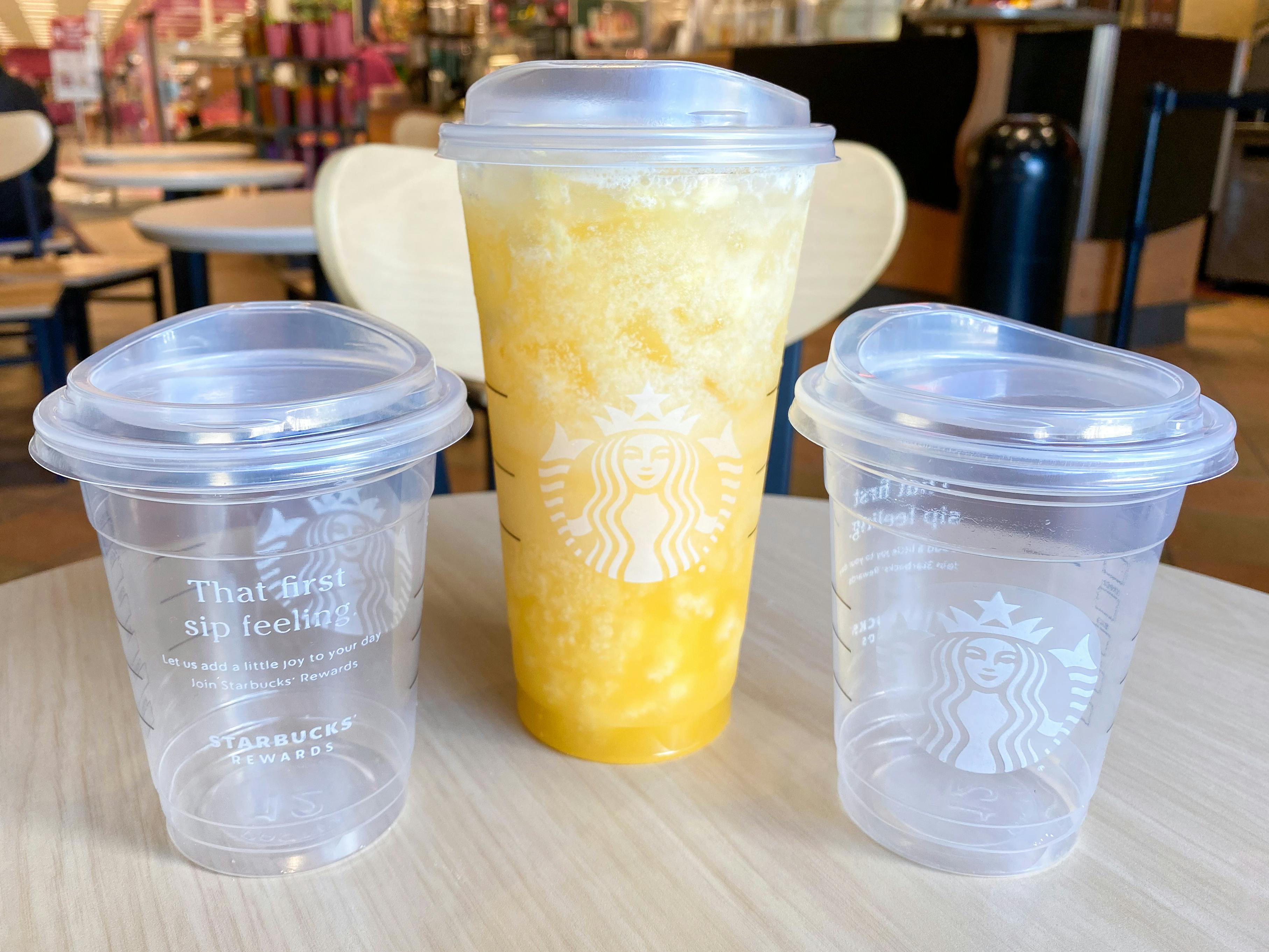 A venti Paradise drink from Starbucks sitting on a table between two empty tall cups inside a Starbucks.