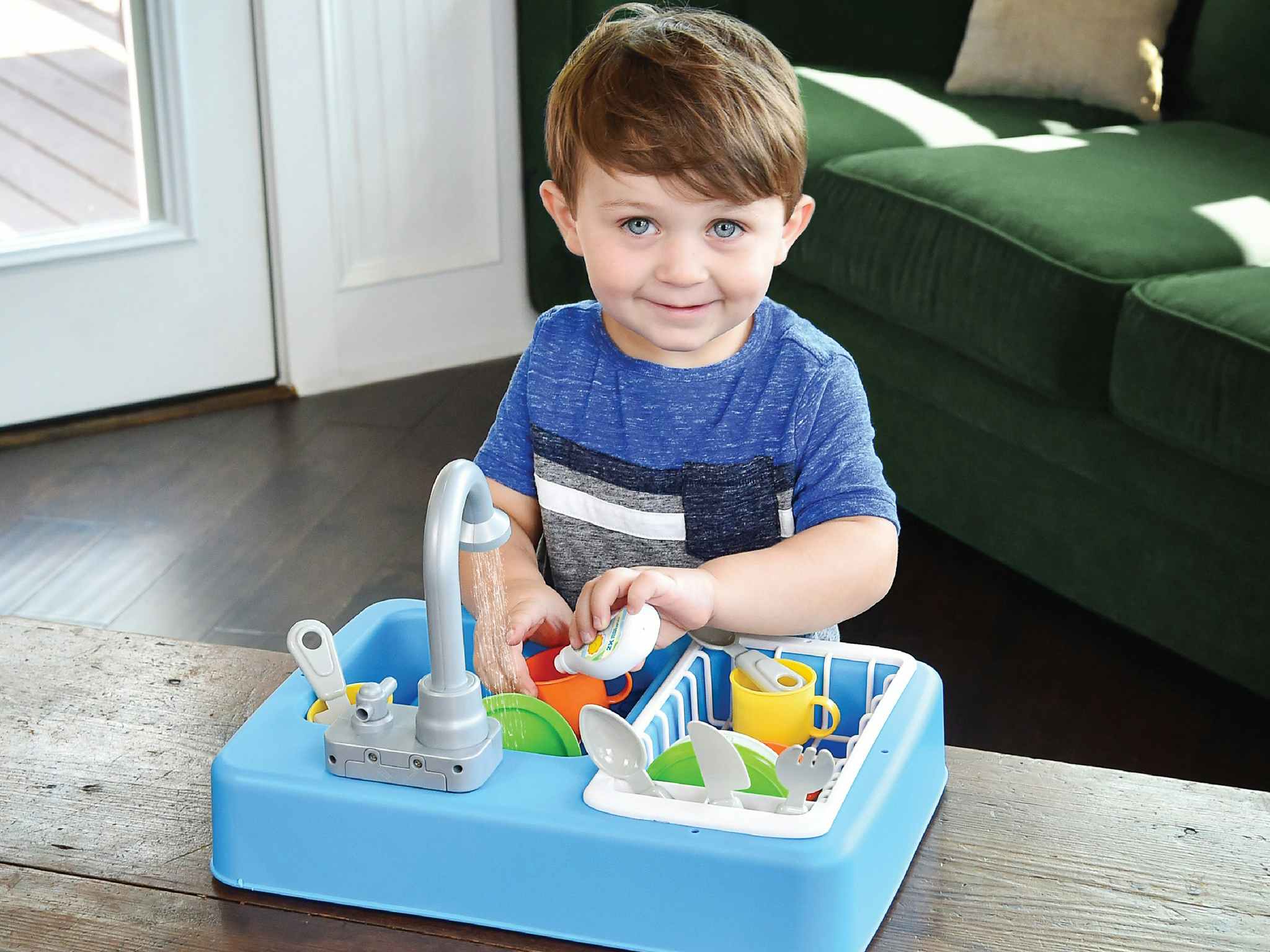 A little boy playing with a Sunny Days Entertainment Kitchen Sink Play Set with Running Water on a table.