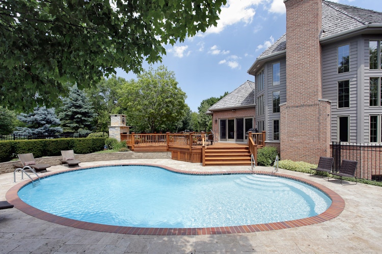 A backyard in-ground swimming pool with some lounge chairs around it.
