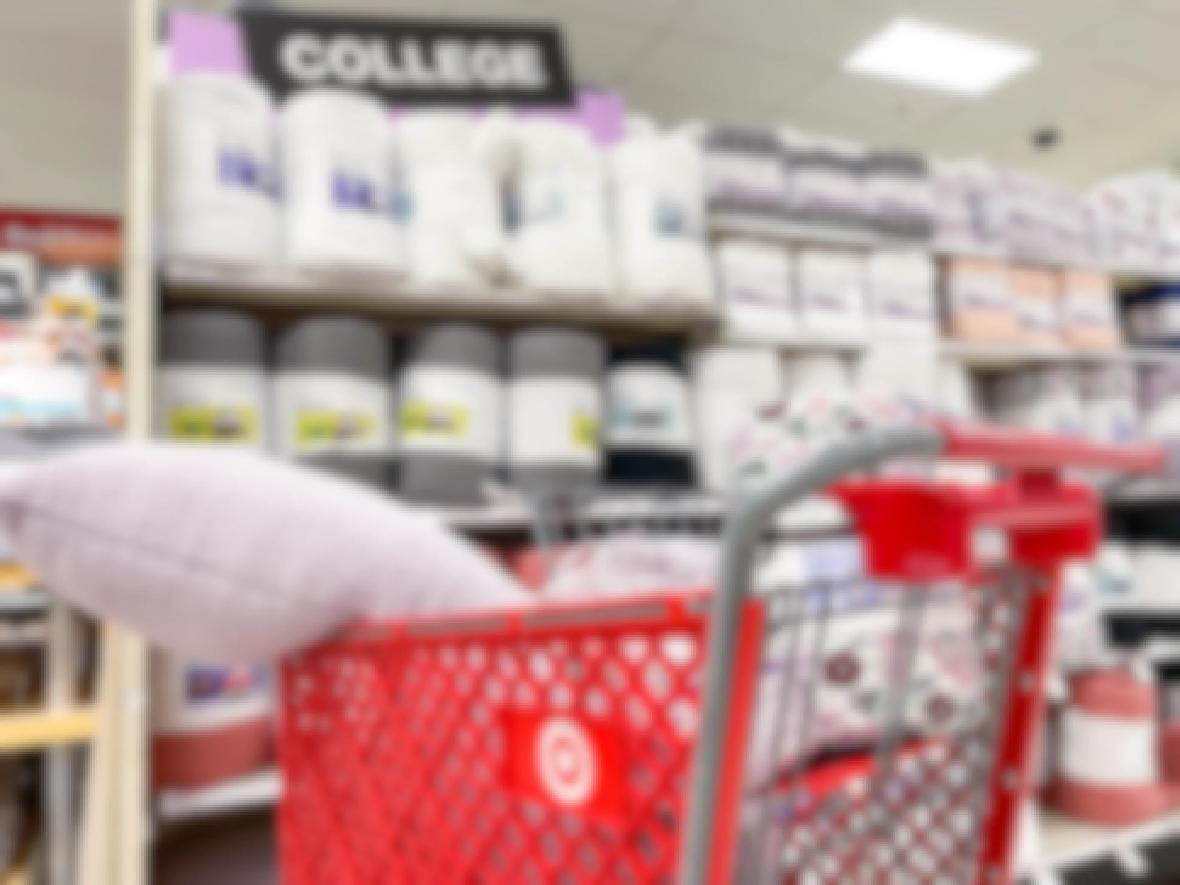 A Target shopping cart filled with bedding items parked in front of a shelf in the College Shop section in Target.