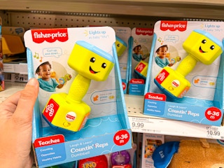 A Fisher-Price children's dumbbell toy held in front of the Fisher-Price shelf with a price tag of 9.99
