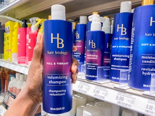 A person's hand taking a bottle of Hair Biology Biotin Volumizing Shampoo from a shelf at Target.