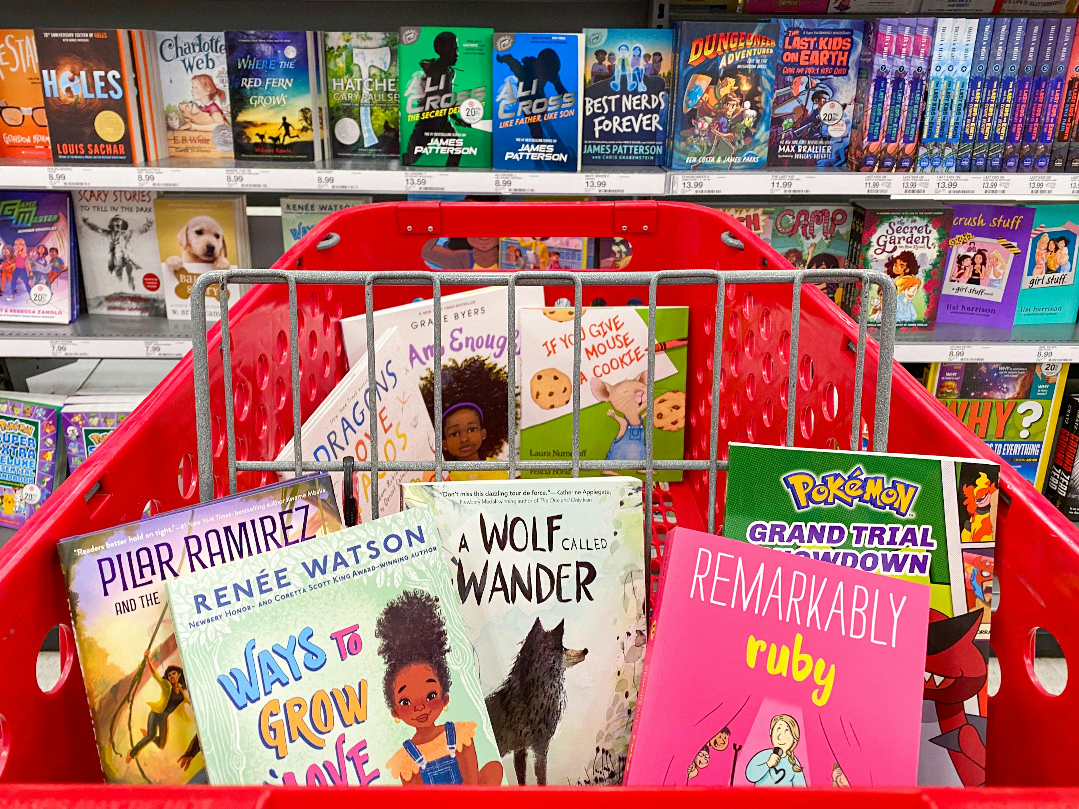 A Target shopping cart filled with kids books parked in front of a shelf of books at Target.