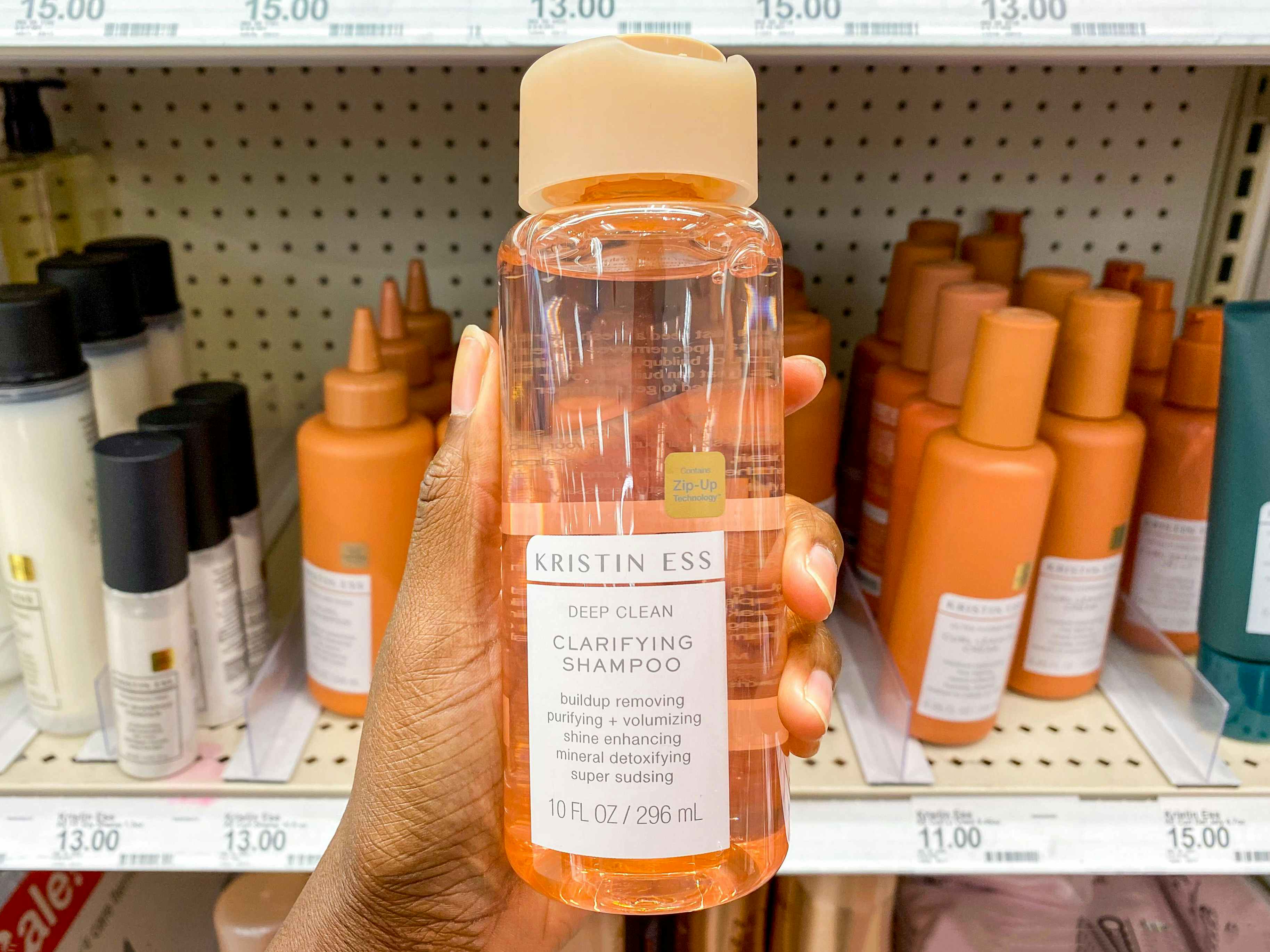 A person's hand holding a bottle of Kristin Ess Deep Clean Clarifying Shampoo in the haircare aisle at Target.