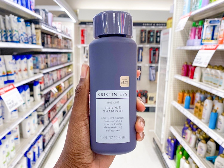 A person's hand holding a bottle of Kristin Ess The One Purple Shampoo in the haircare aisle at Target.