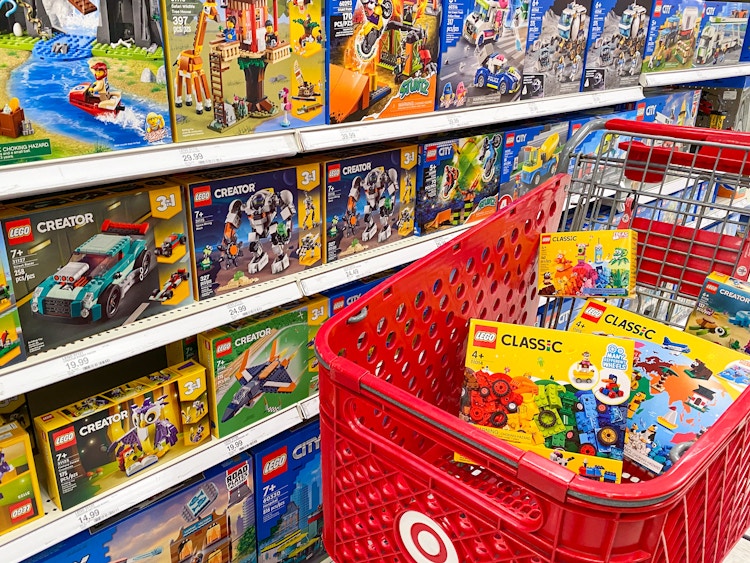 A Target shopping cart full of LEGO toys parked next to a shelf stocked with LEGO toys at Target.