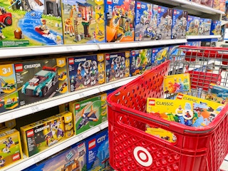 A Target shopping cart full of LEGO toys parked next to a shelf stocked with LEGO toys at Target.