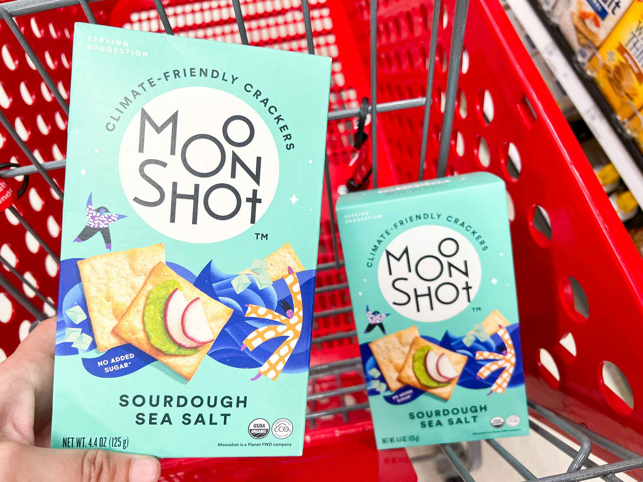 A person putting a box of moonshot crackers into a target shopping cart