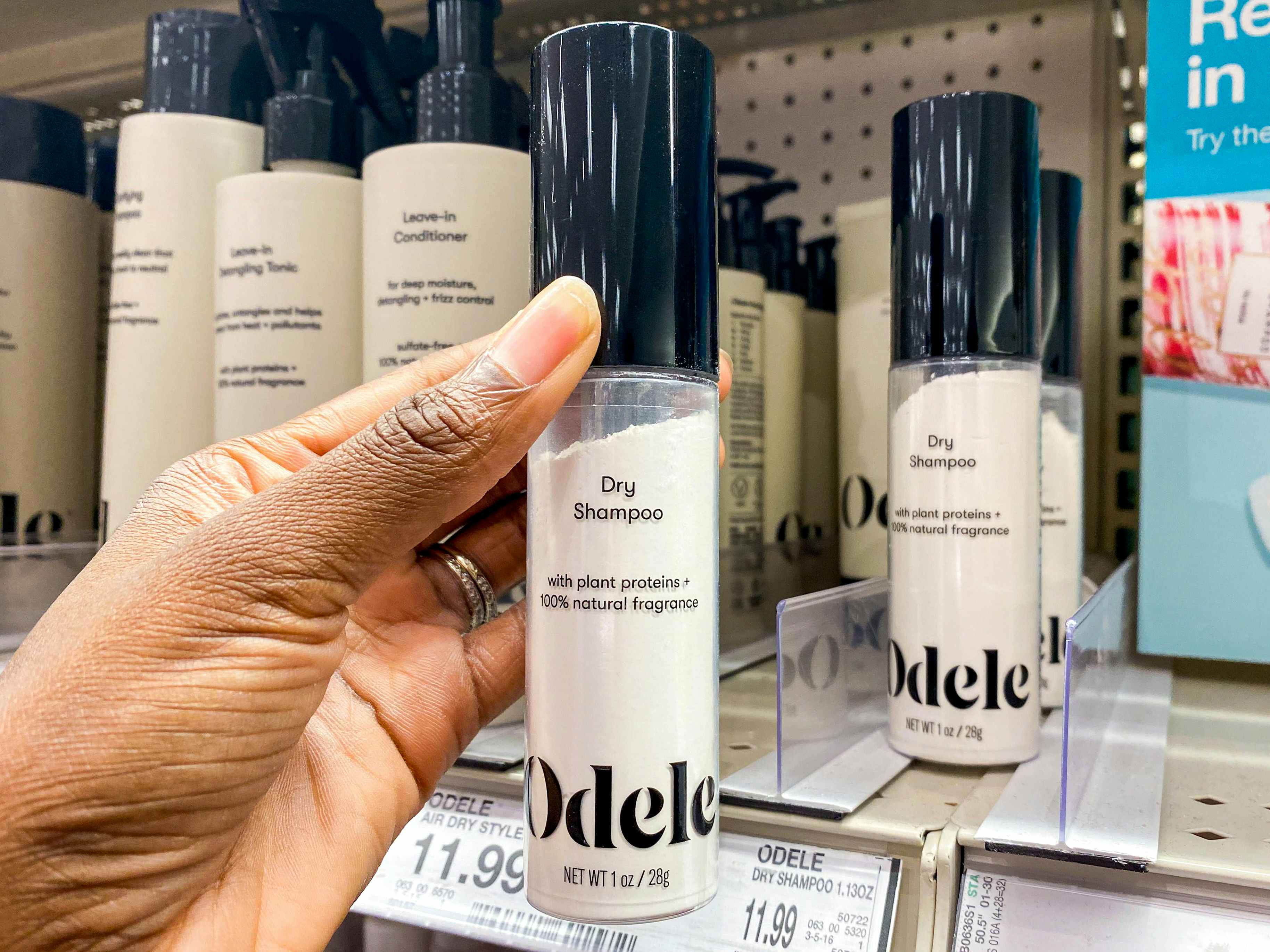 A person's hand taking a bottle of Odele Dry Shampoo from a shelf at Target.