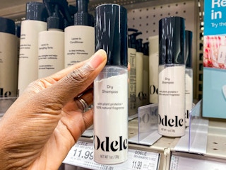 A person's hand taking a bottle of Odele Dry Shampoo from a shelf at Target.