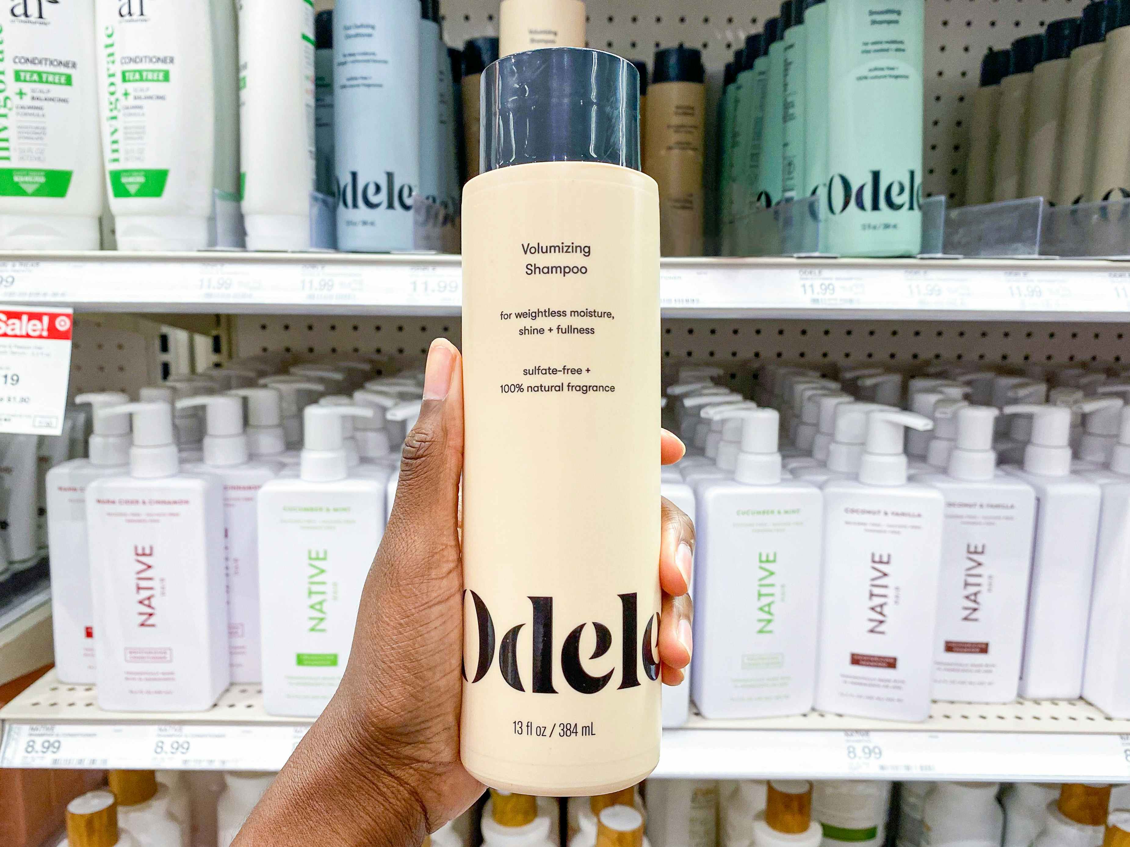 A person's hand holding a bottle of Odele volumizing shampoo in the haircare aisle at Target.