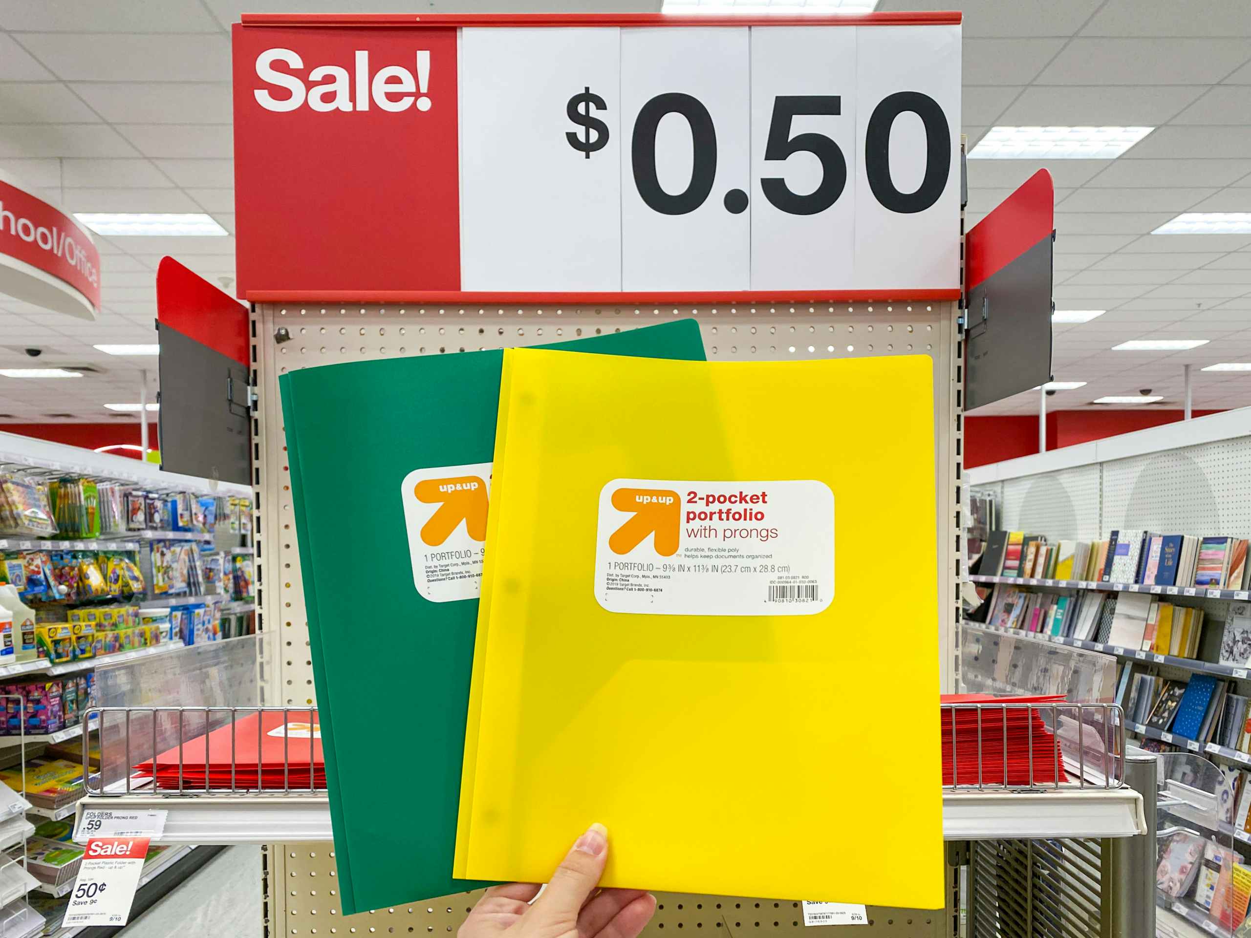 A person's hand holding up two Up&Up brand school folders in front of a 50 cent sale sign at Target.