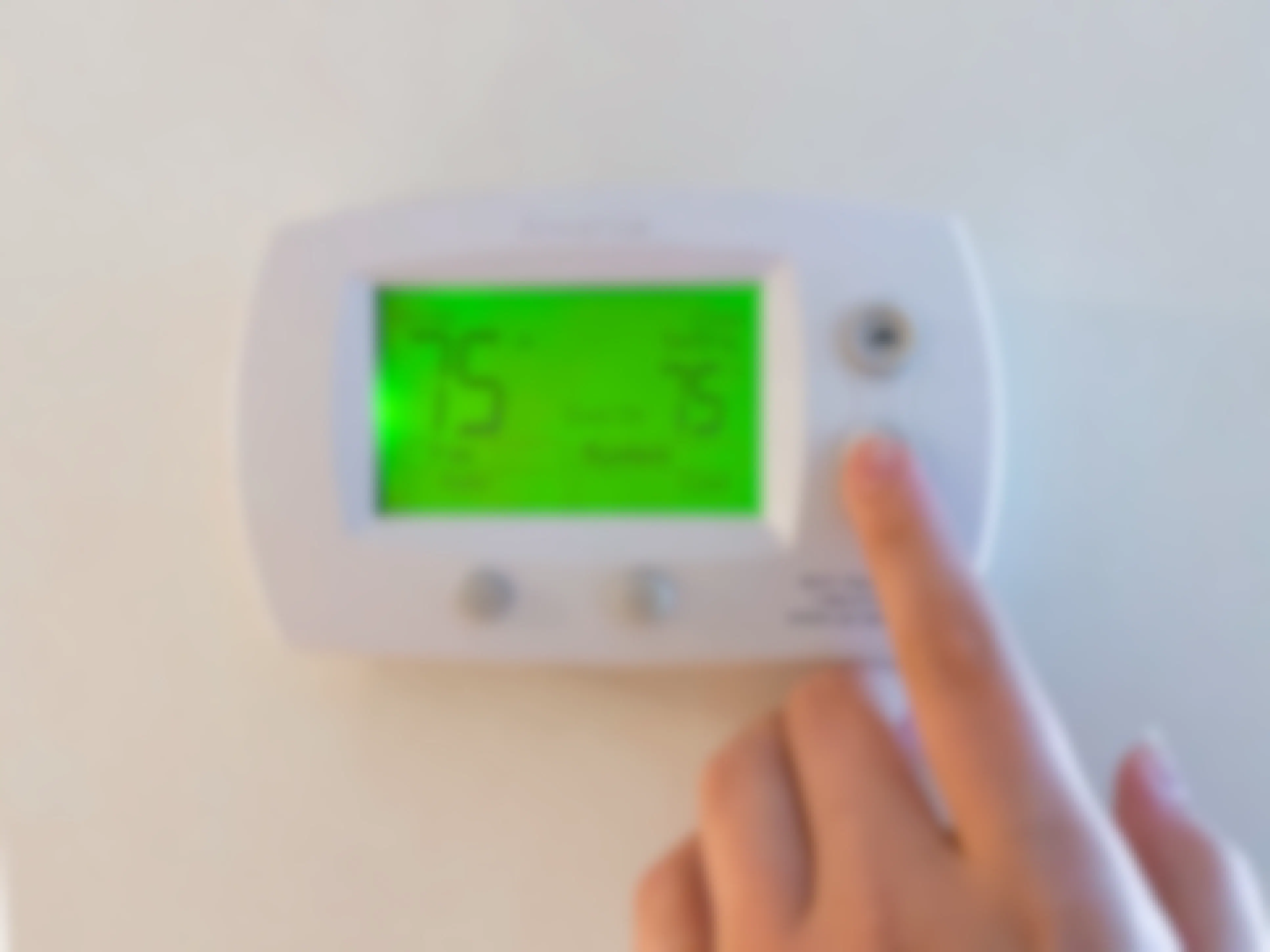 A person's hand going to turn the temperature down on the thermostat which shows 75 degrees Fahrenheit.