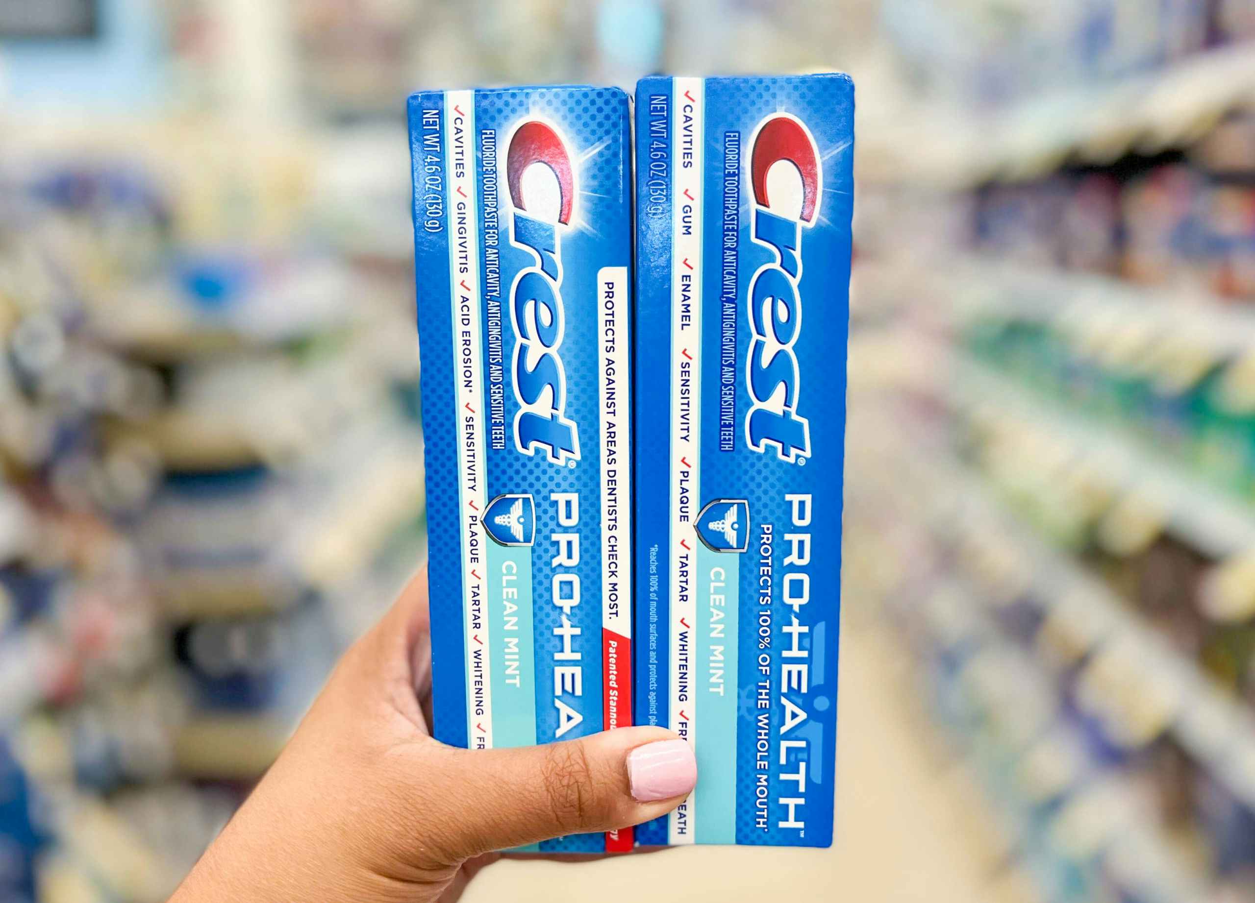 Hand holding two boxes of Crest Pro-Health toothpaste