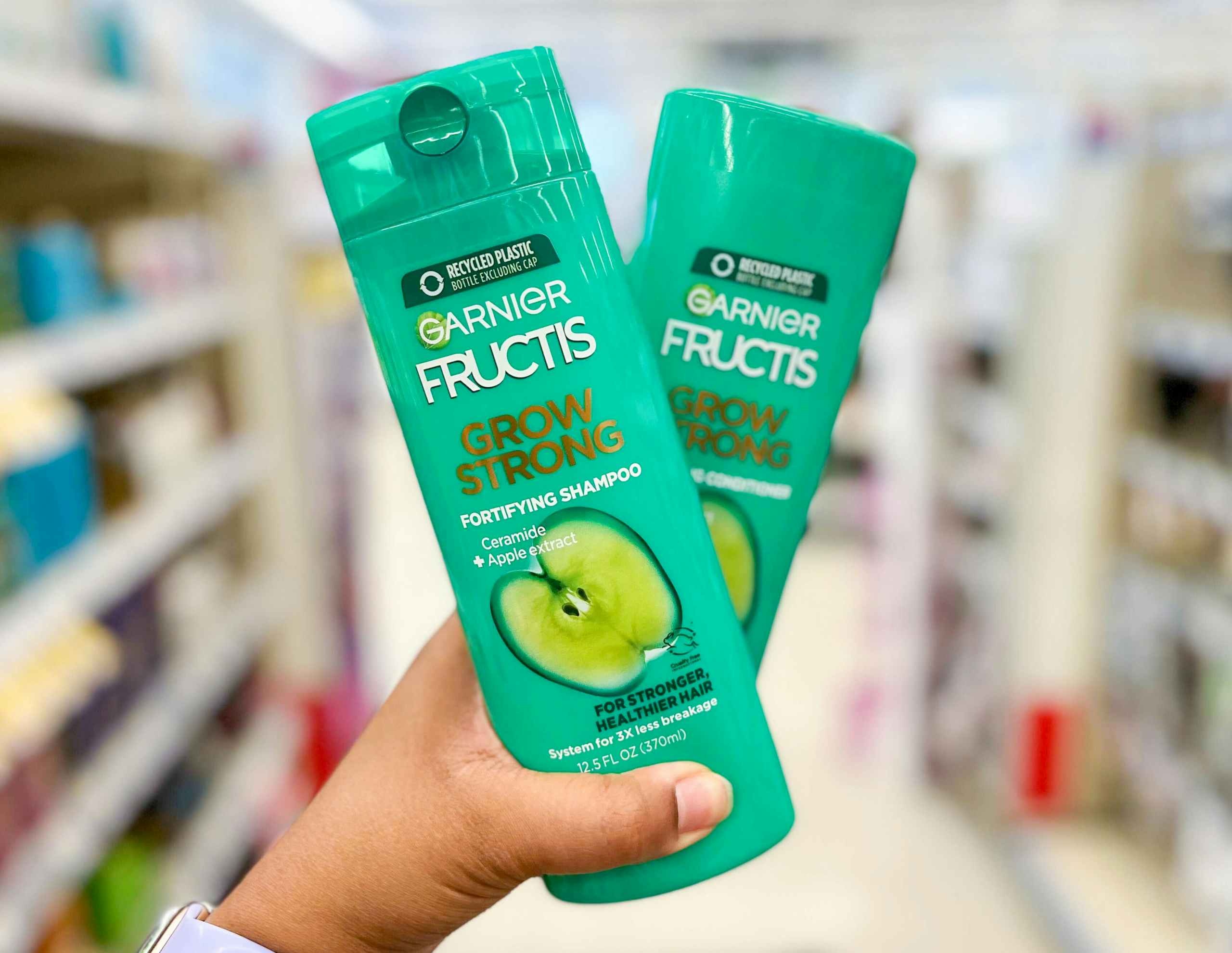 hand holding a bottle of Garnier Fructis Grow Strong shampoo and conditioner in aisle