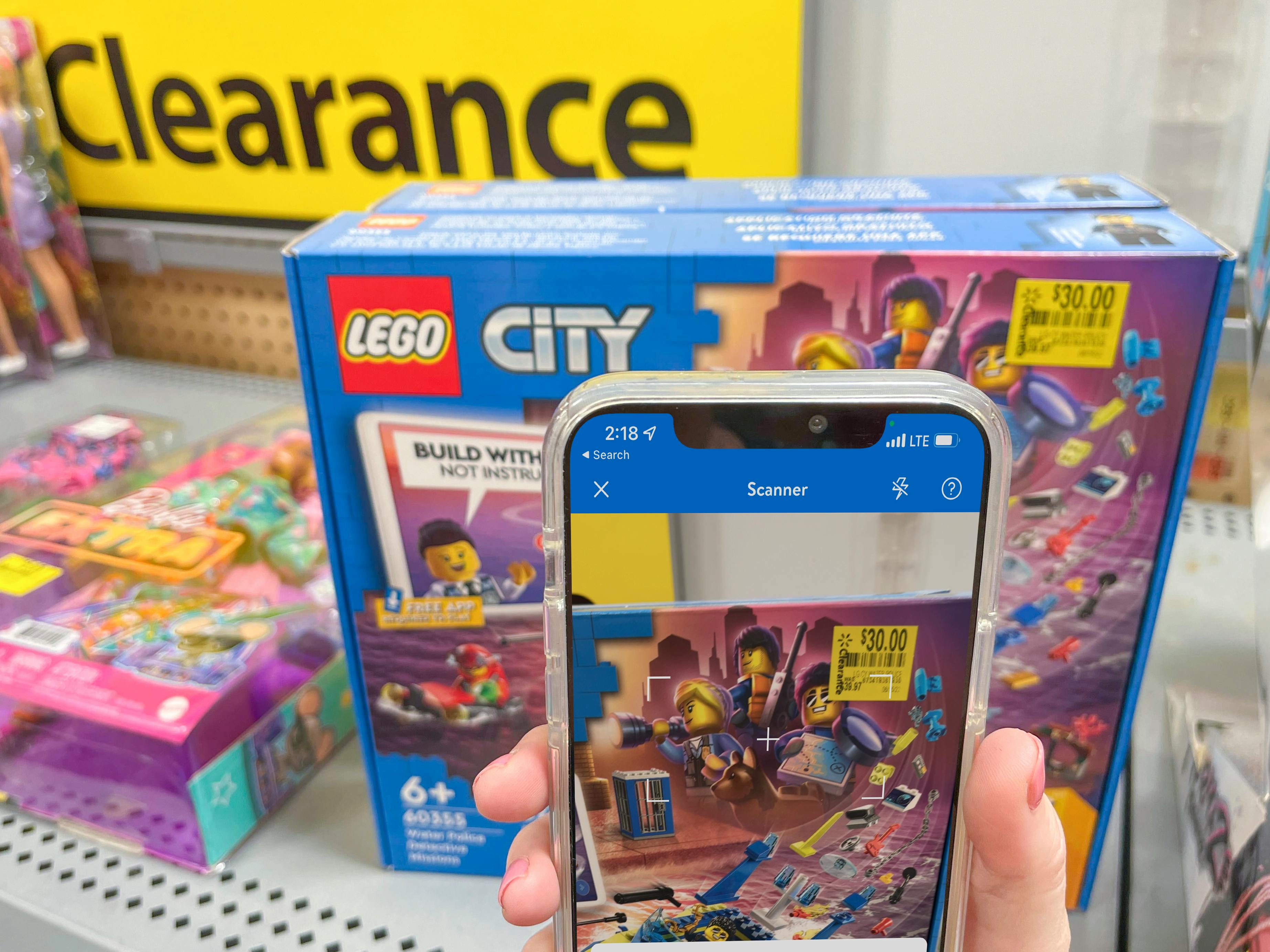 A person's hand holding up their cellphone, using the Walmart app to scan the price of a toy on a clearance shelf.